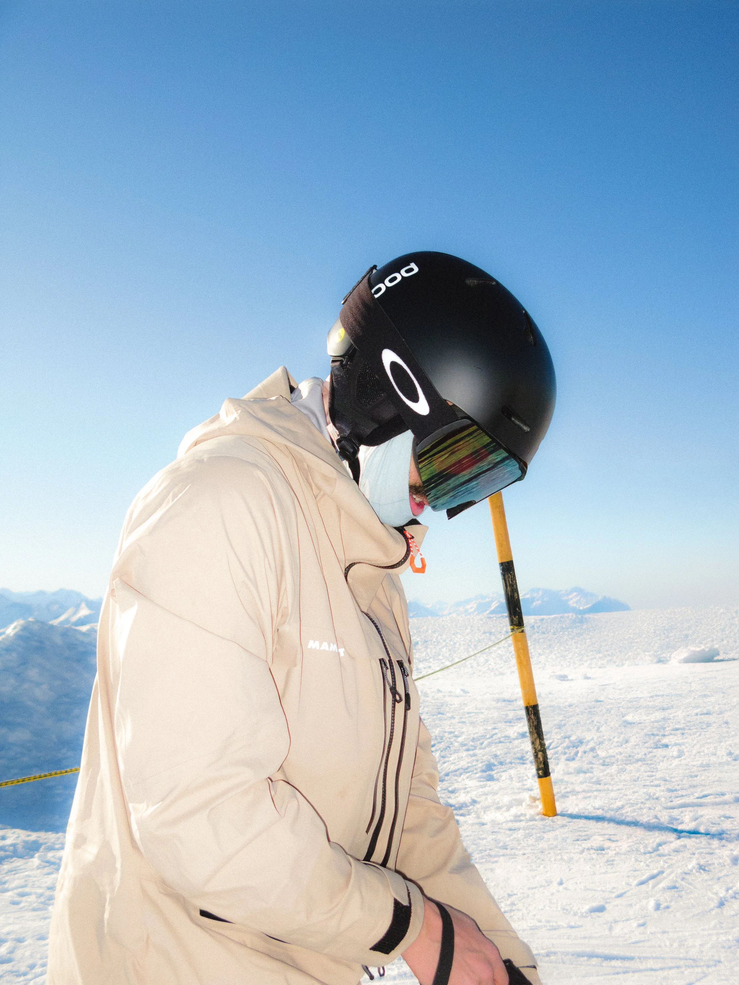 Personne portant un casque de ski et des lunettes de soleil sur une montagne enneigée.