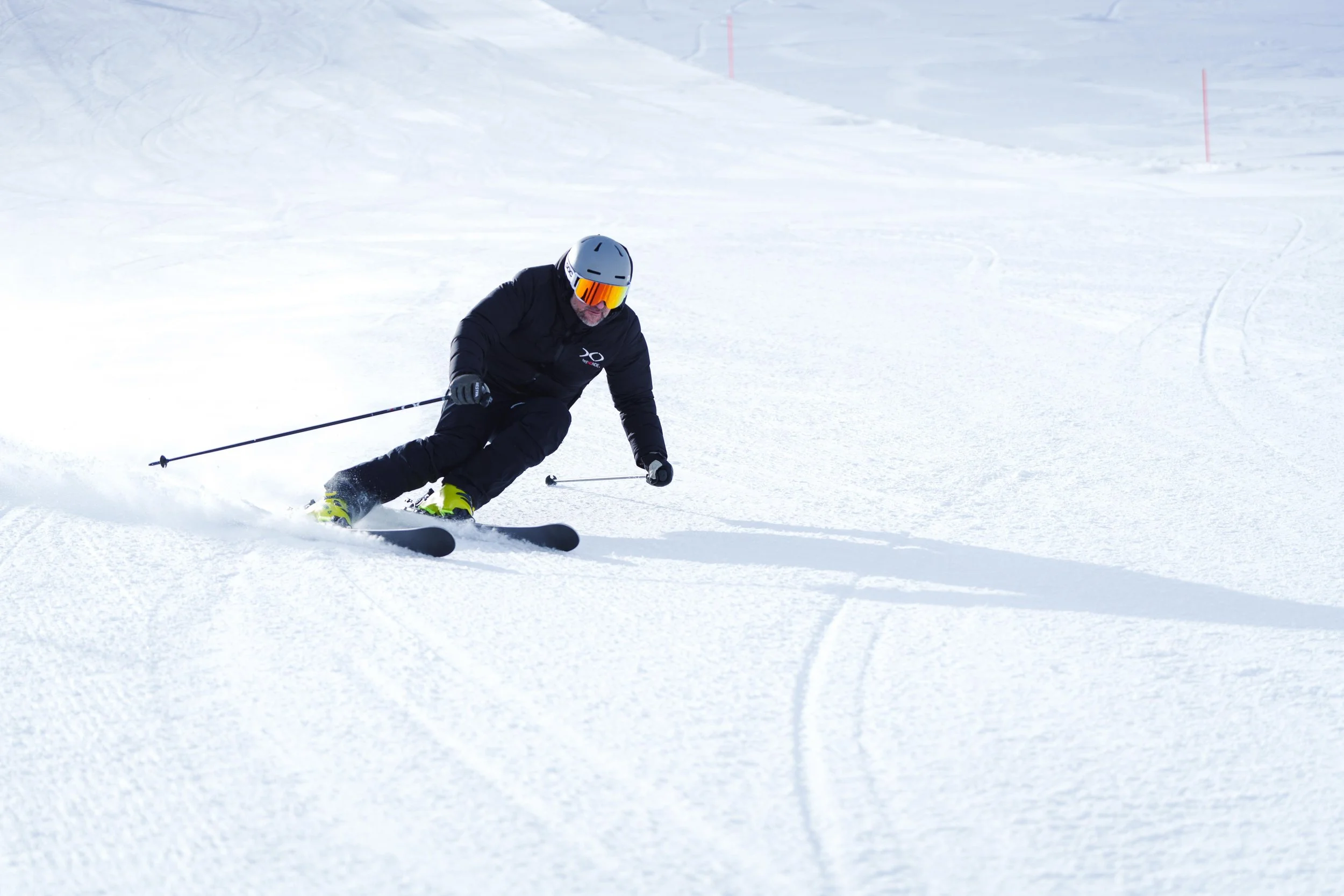 Un skieur en tenue noire et casque gris, descendant une pente enneigée, tenant des bâtons de ski.