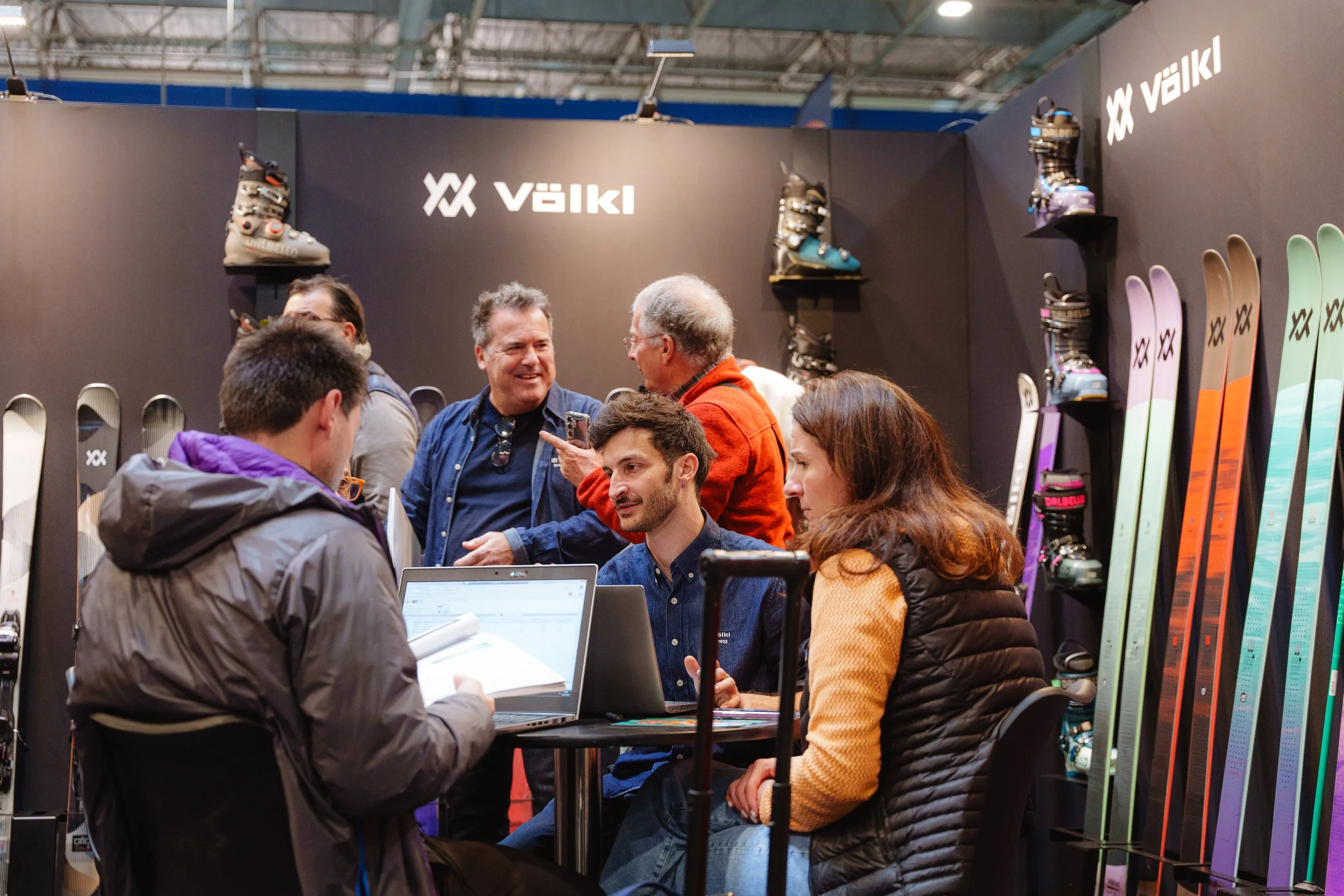 Personnes discutant dans un stand de salon de ski Volkl, avec skis et chaussures exposés.