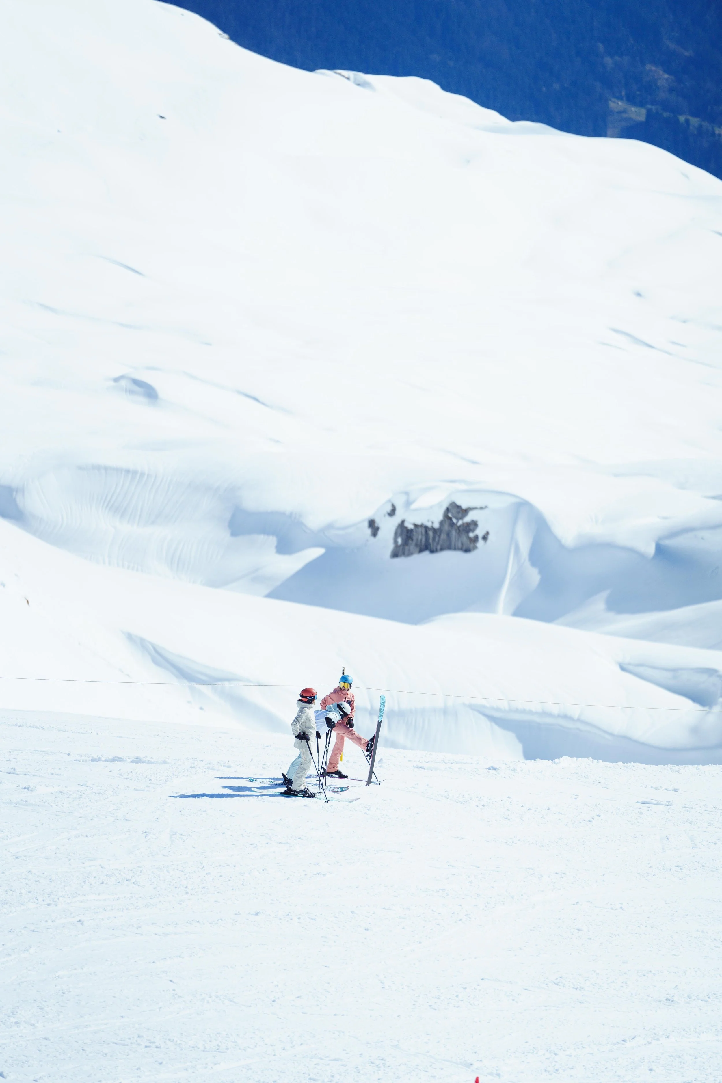 Deux skieurs sur une piste enneigée, avec des montagnes couvertes de neige en arrière-plan.