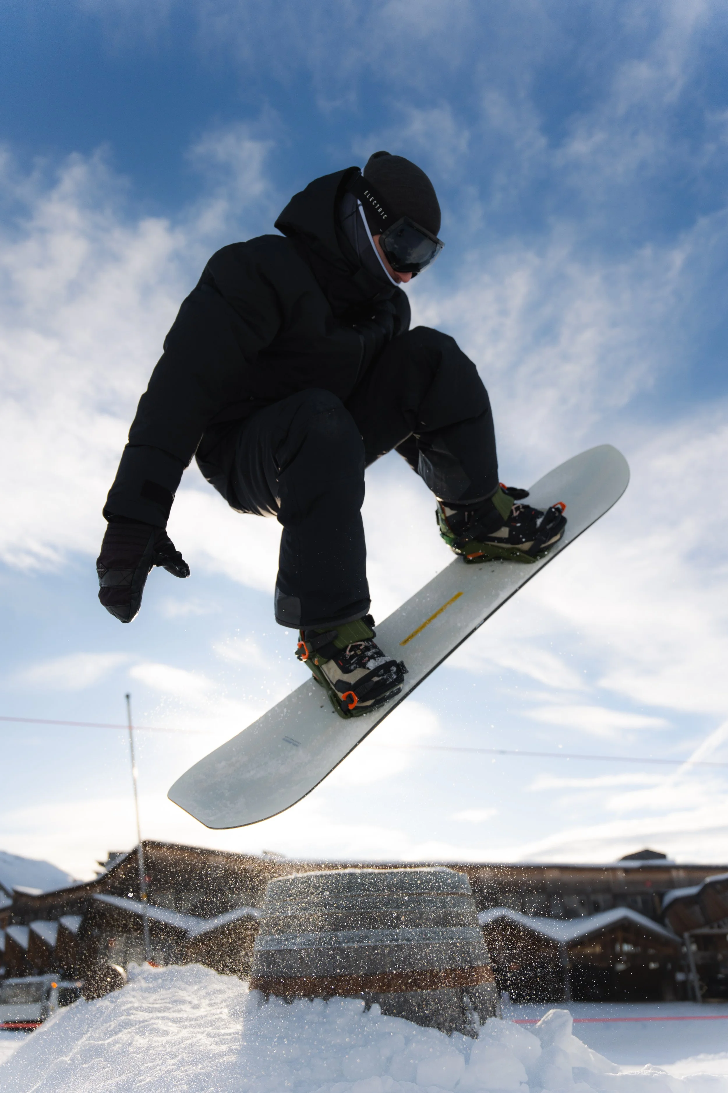 Un snowboardeur effectue un saut dans un paysage enneigé sous un ciel bleu.