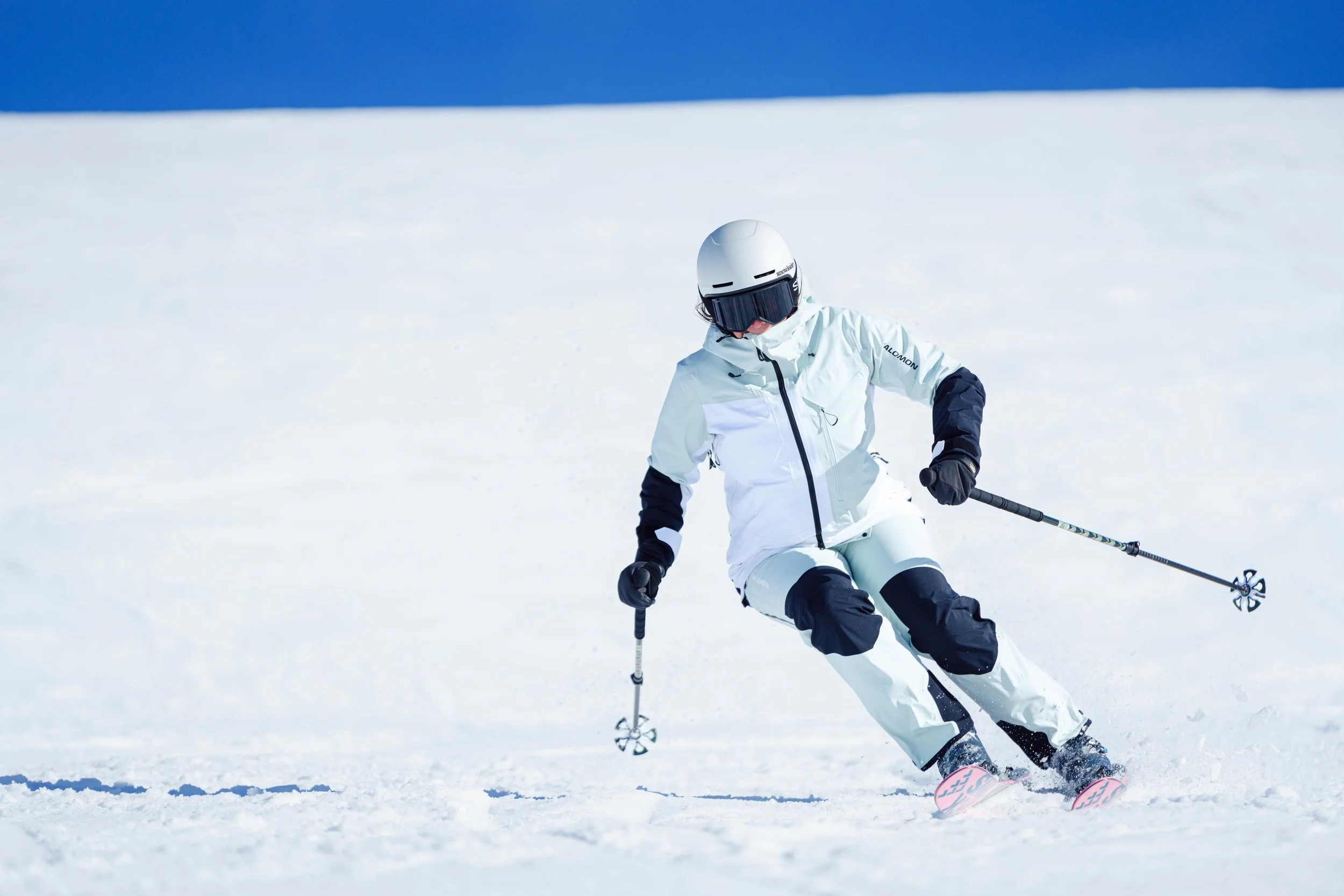 Personne en train de skier sur une piste enneigée avec un ciel bleu en arrière-plan.