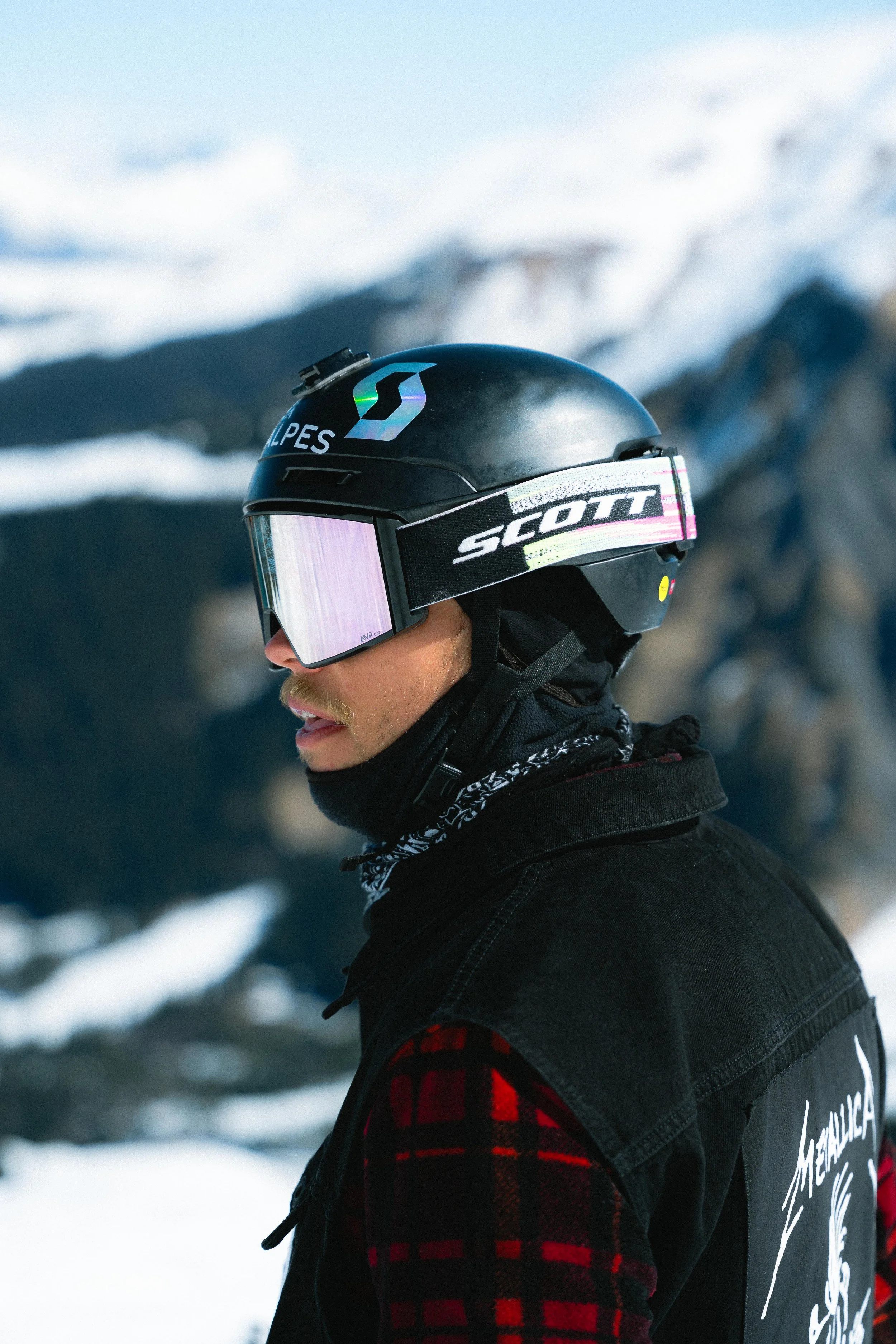 Personne portant un casque de ski avec des lunettes de protection, arrière-plan montagneux enneigé.