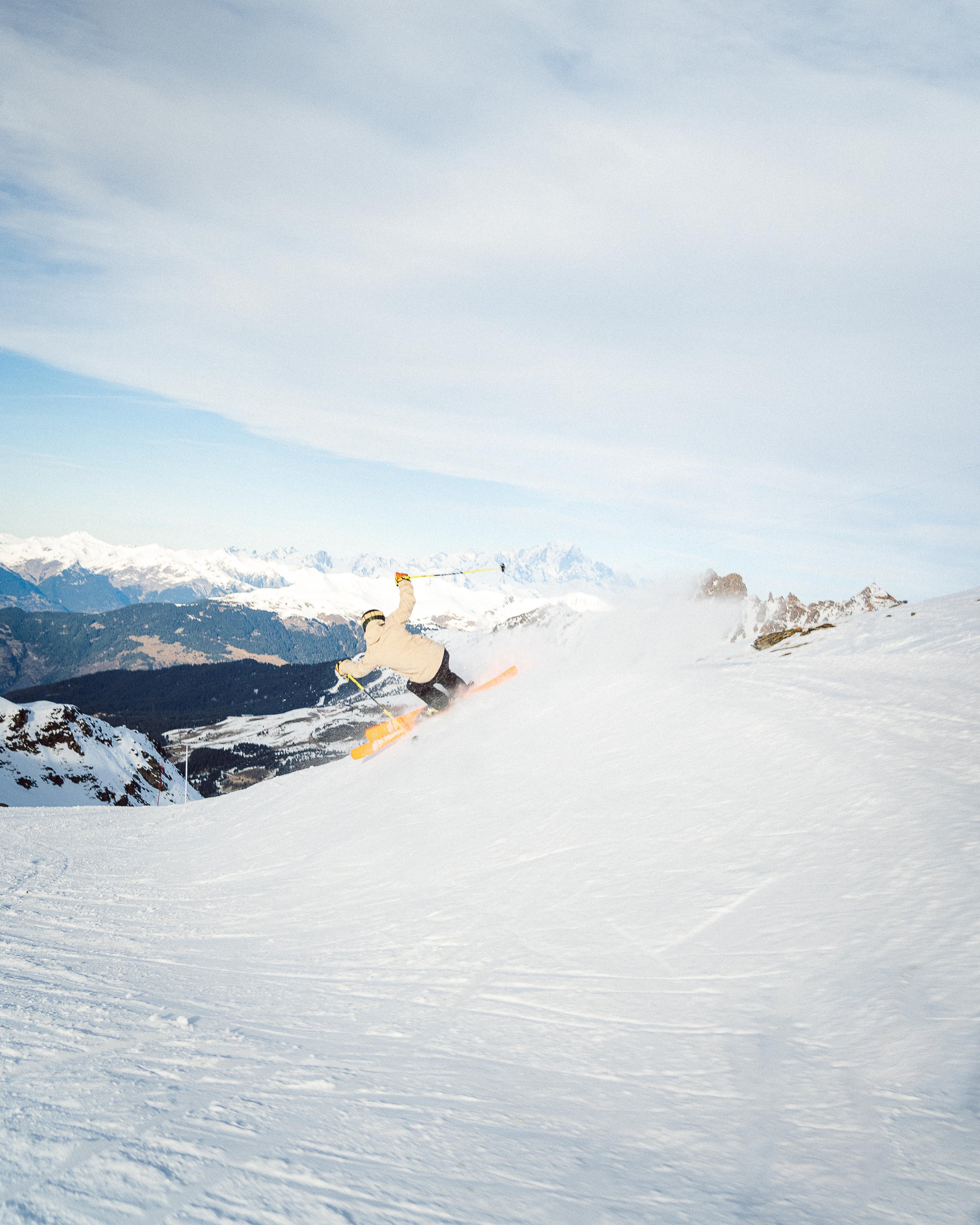 Un skieur effectuant une descente sur une piste enneigée avec un panorama de montagnes en arrière-plan.