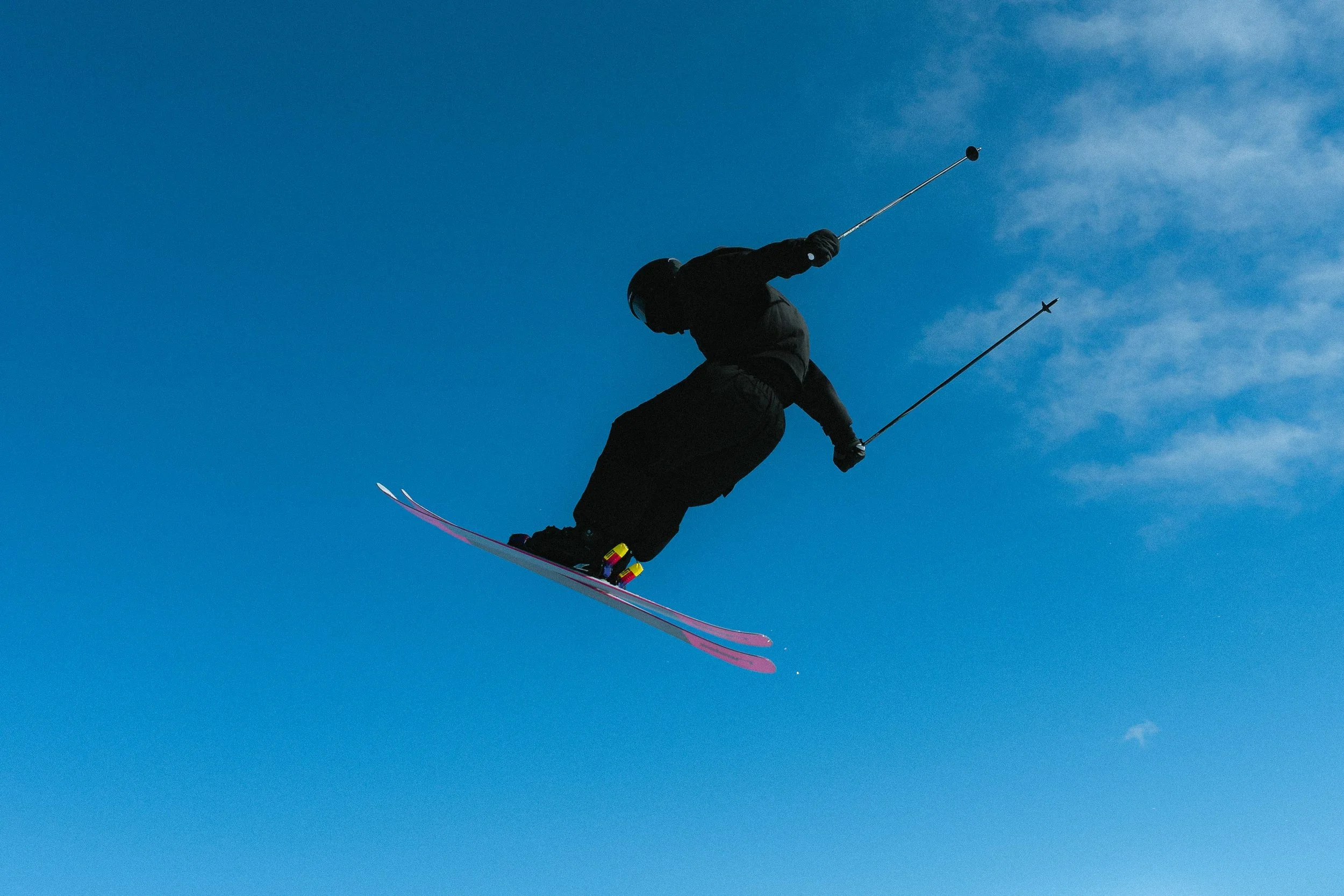Skieur en plein saut sous un ciel bleu avec des bâtons de ski.