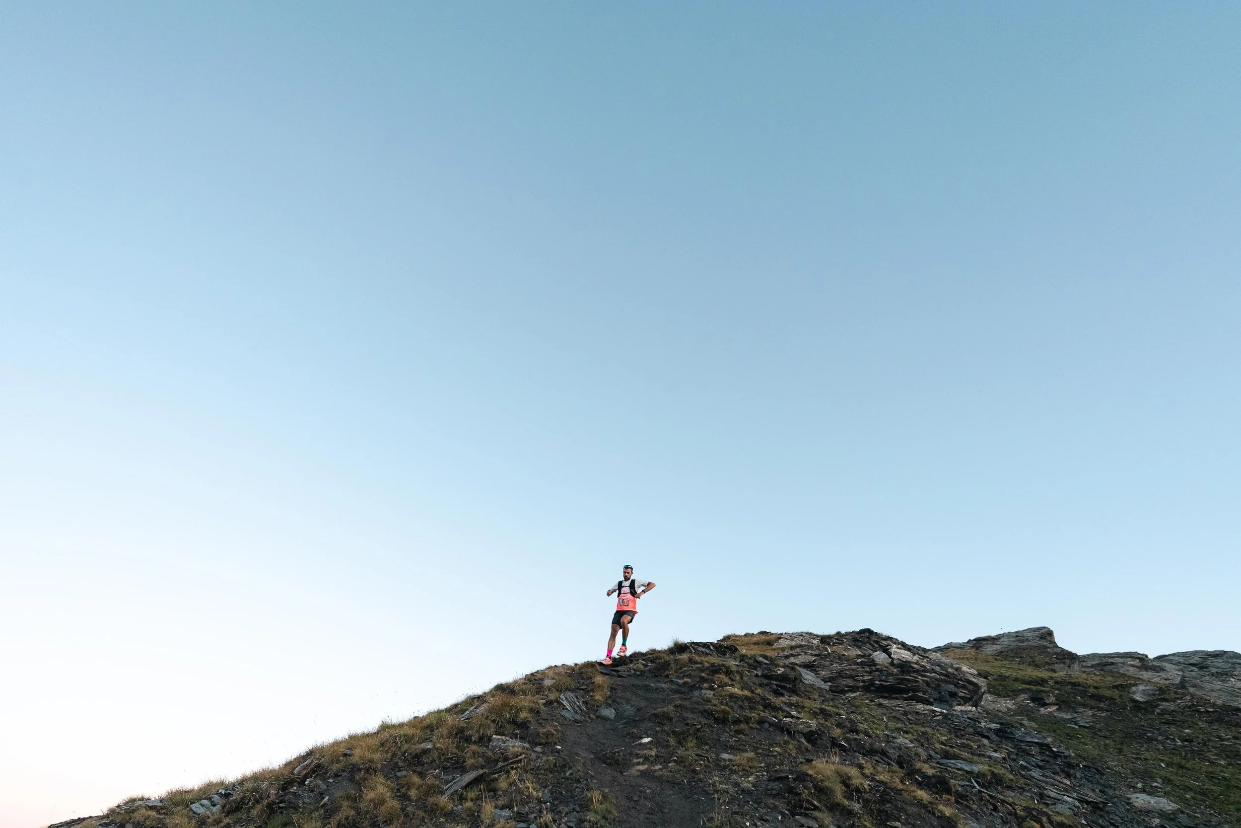 Coureur vêtu de vêtements sportifs se tenant sur une colline rocheuse sous un ciel bleu.
