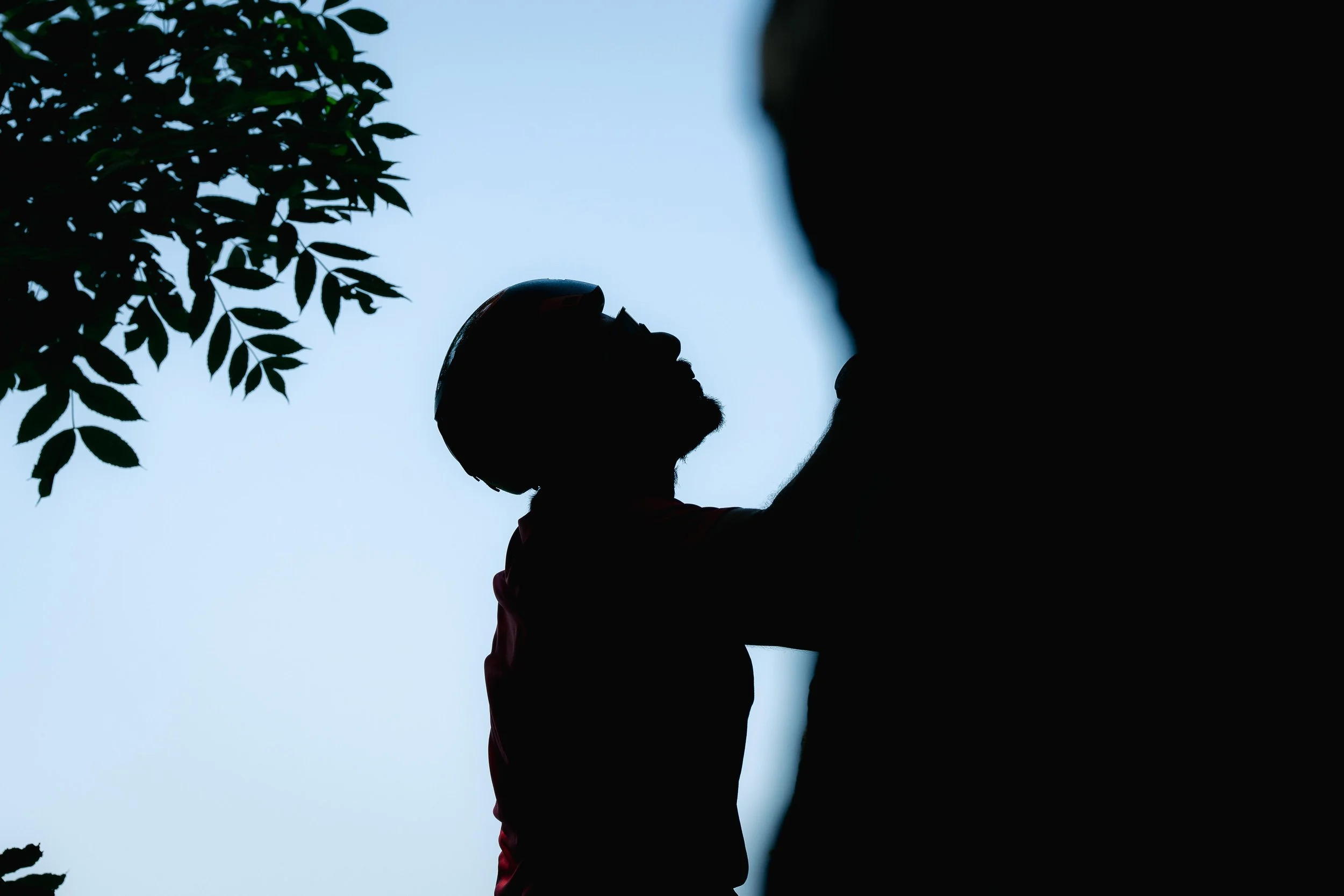 Silhouette d'une personne escaladant un mur avec des feuilles d'arbre en arrière-plan.
