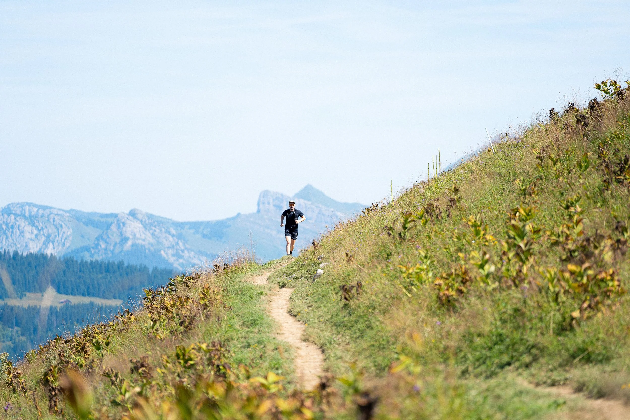 Un homme courant sur un sentier de montagne avec un paysage de collines verdoyantes à l'arrière-plan.