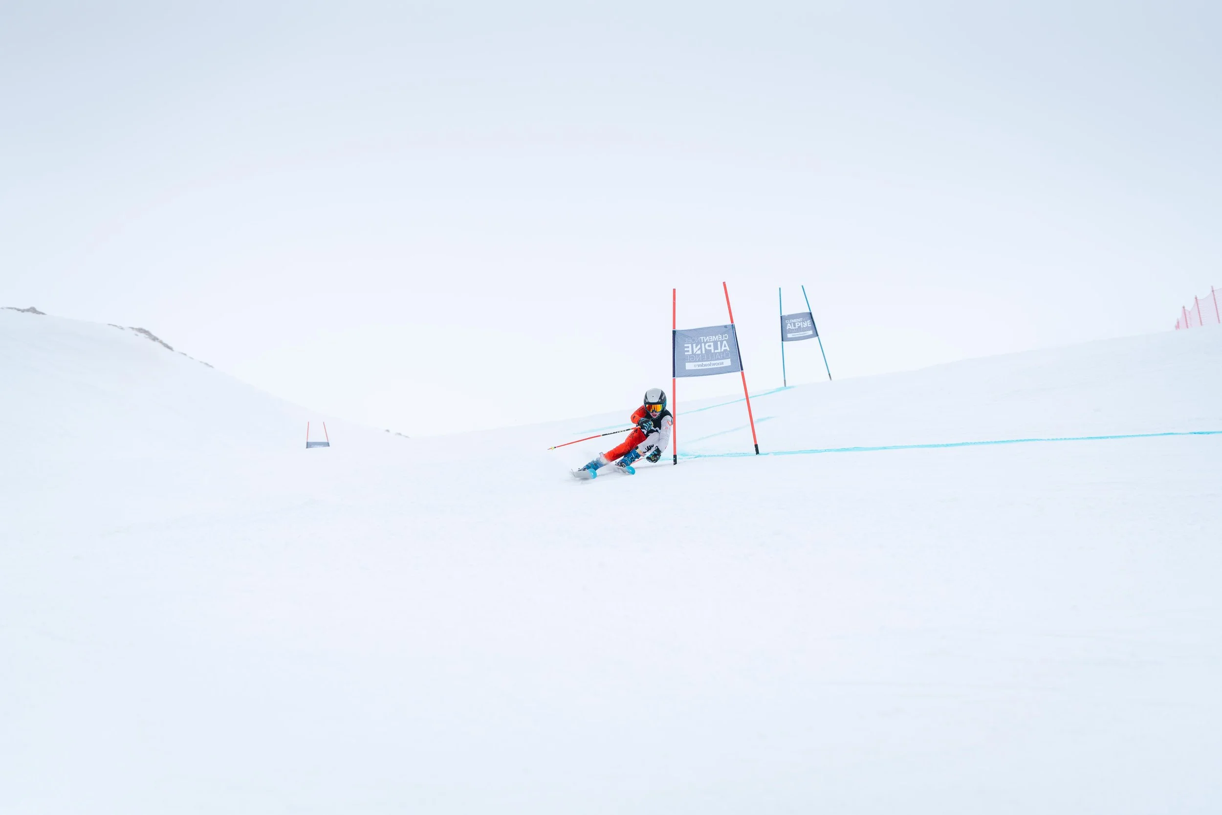 Un skieur en compétition dévale une pente enneigée en slalomant entre des piquets rouges et bleus, sous un ciel gris.