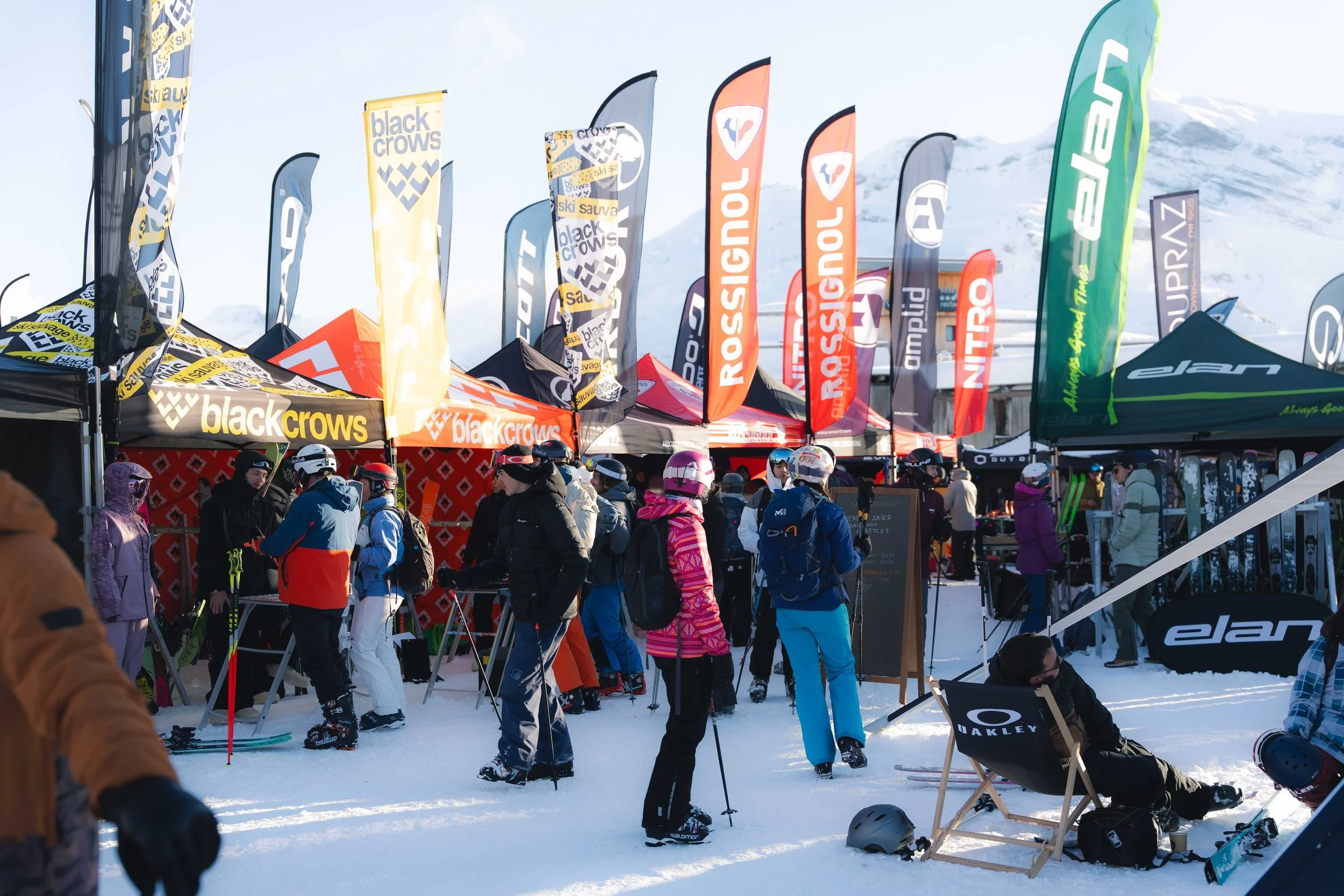 Événement de ski avec tentes de marques de sports d'hiver, skieurs, et drapeaux colorés sur la neige.