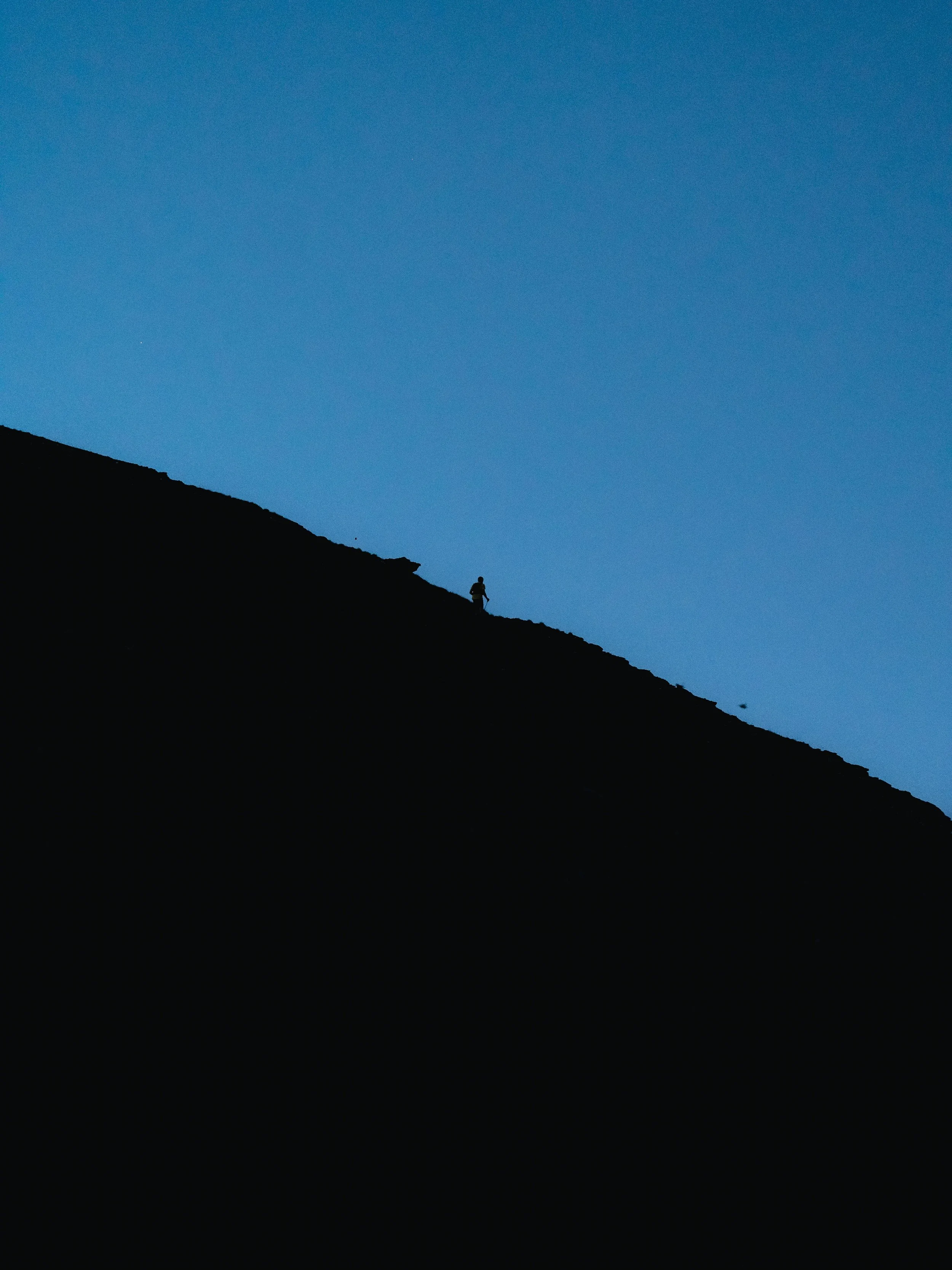 Silhouette d'une personne sur une colline sous un ciel bleu.