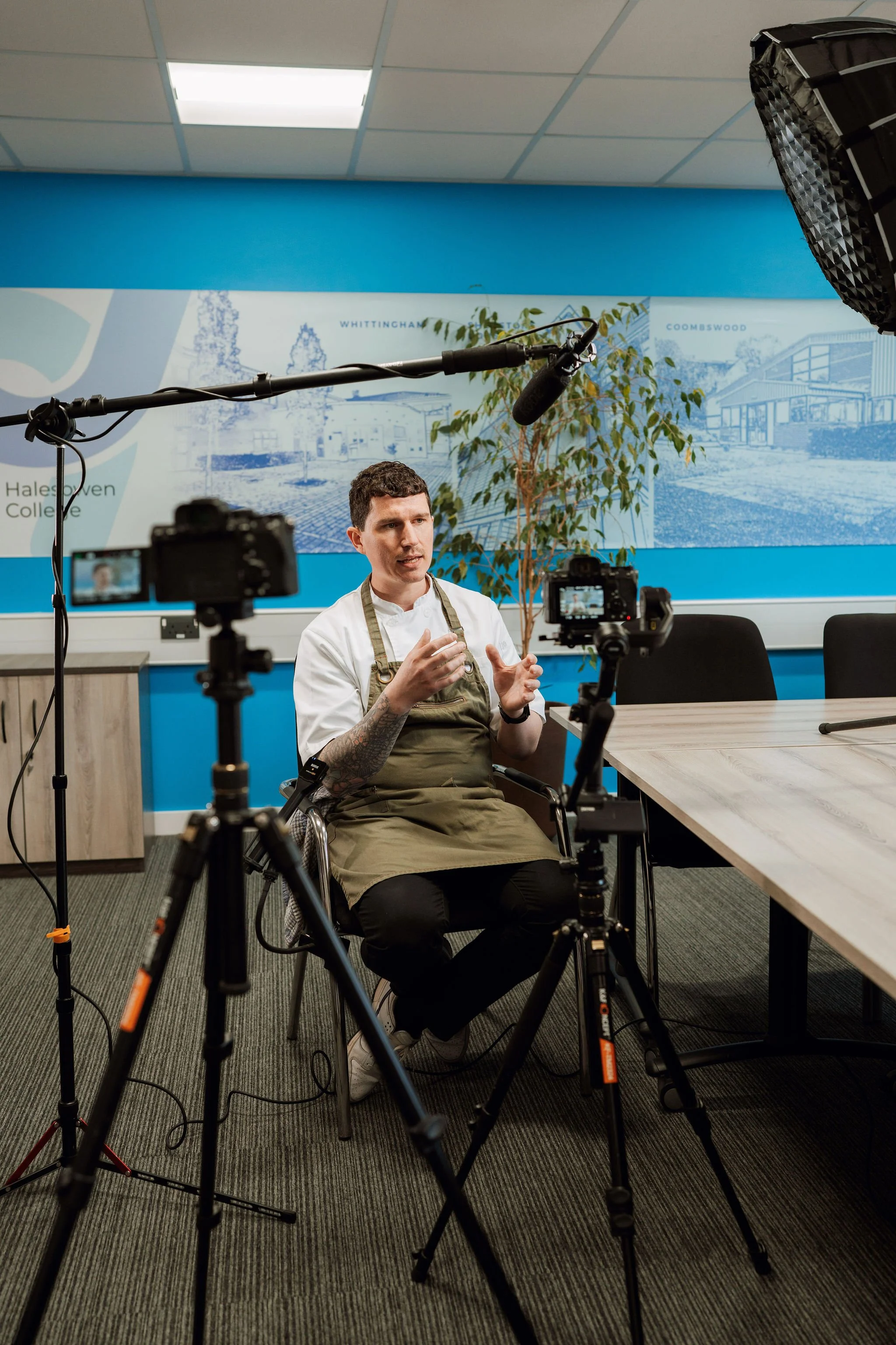 man wearing chef outfit sat in front of camera gesticulating with his handss