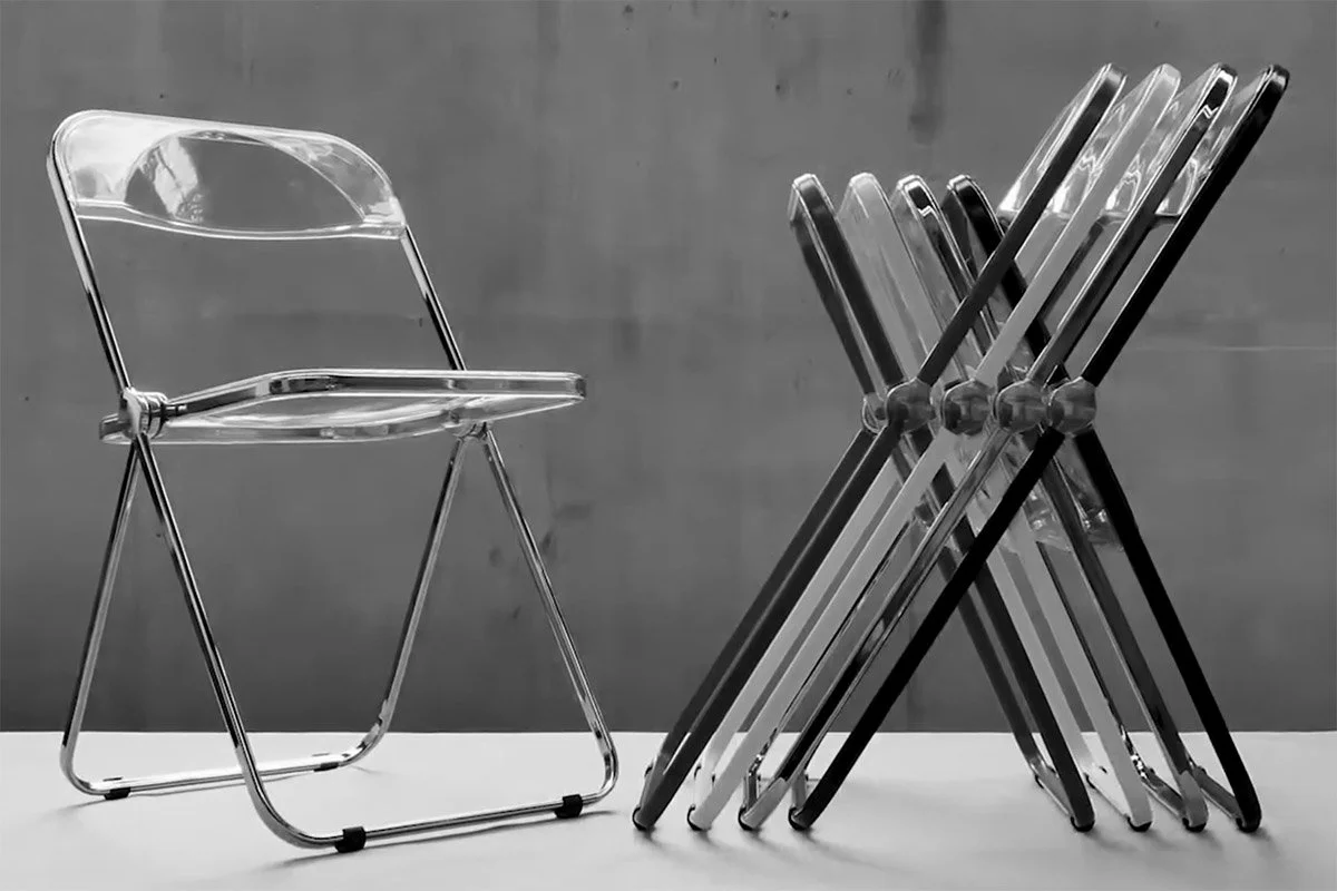 A clear plastic plia chair with a metal frame and five translucent folding chairs, all arranged on a white surface against a grey wall.