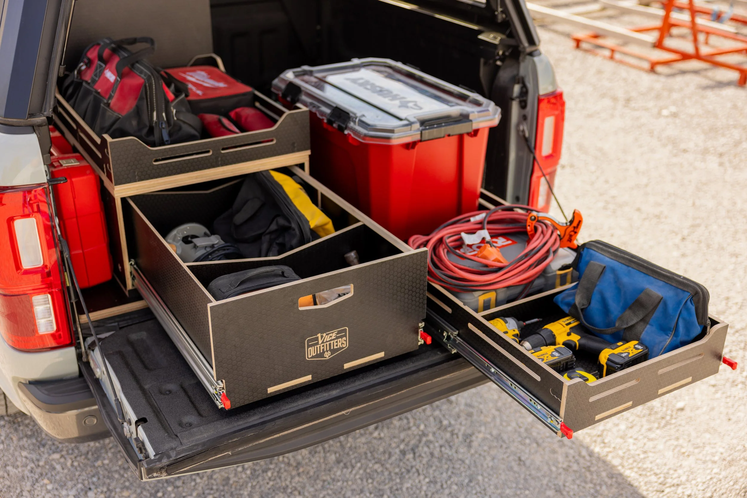 Open truck tailgate showing organized tool and equipment in a VICE Outfitters storage system. Including totes, power tools, extension cords, and gear.