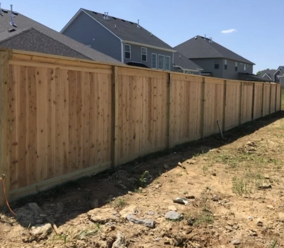 New wooden privacy fence being installed along a backyard, with neighboring houses visible in the background.