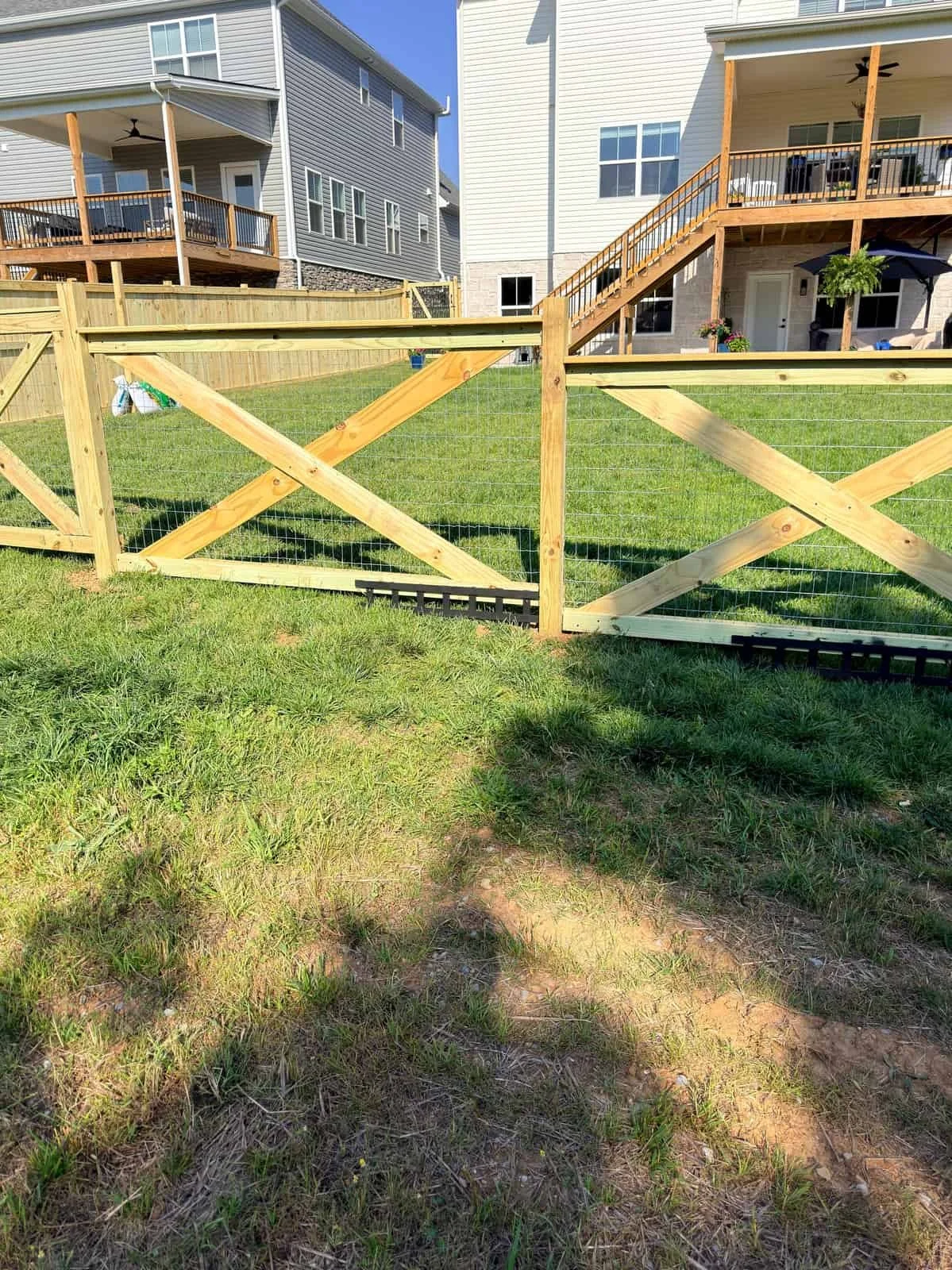 A backyard with green grass, a wooden fence, and two neighboring houses with balconies and stairs leading to the backyard.