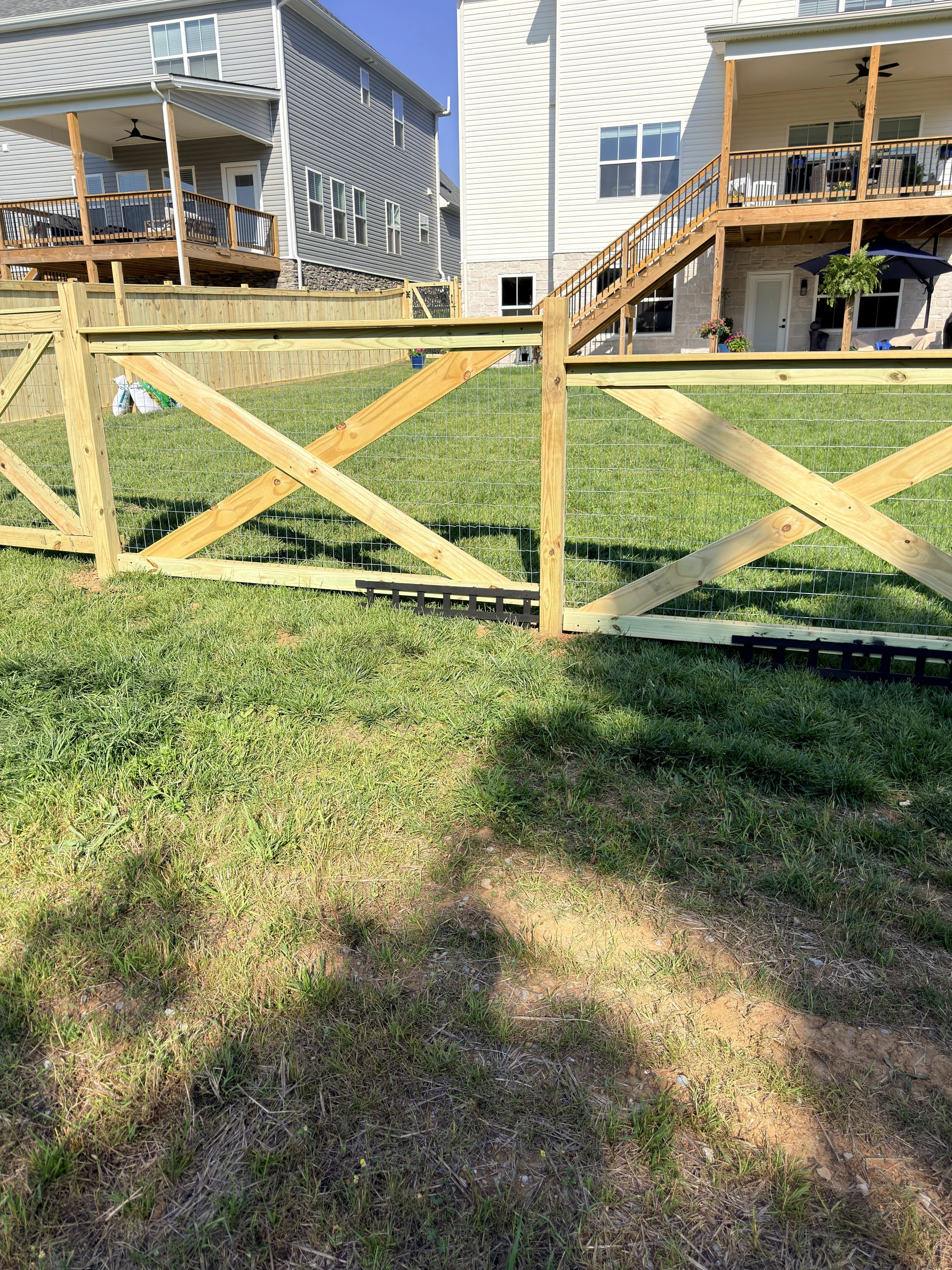 Backyard with green grass, wooden fence, two-story houses with decks, outdoor furniture, and a patio umbrella.