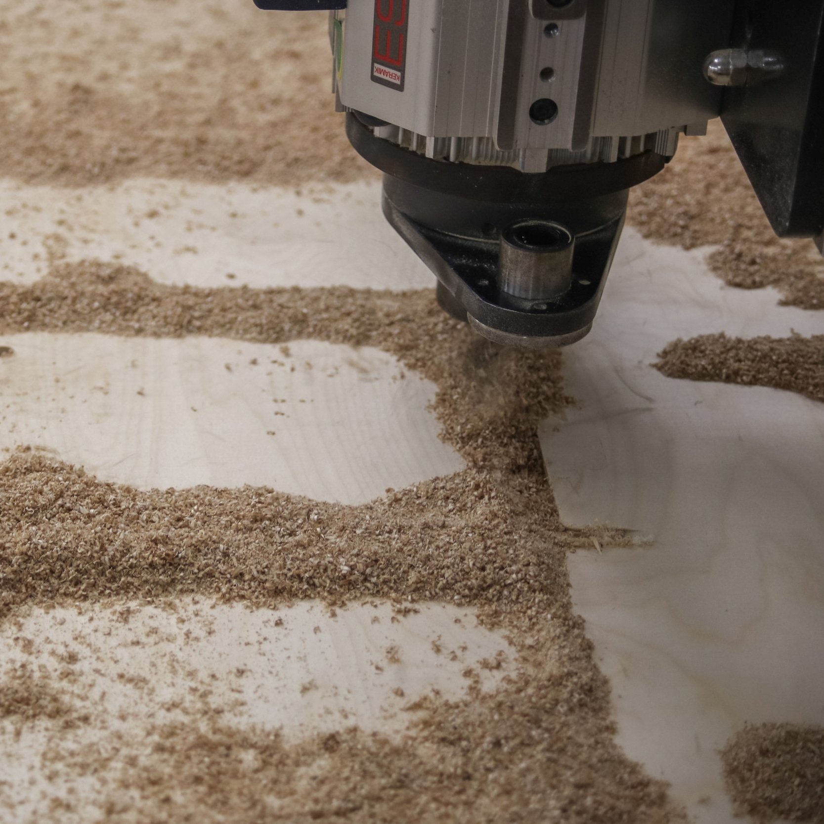 A CNC router carving a design with sawdust on a piece of wood.