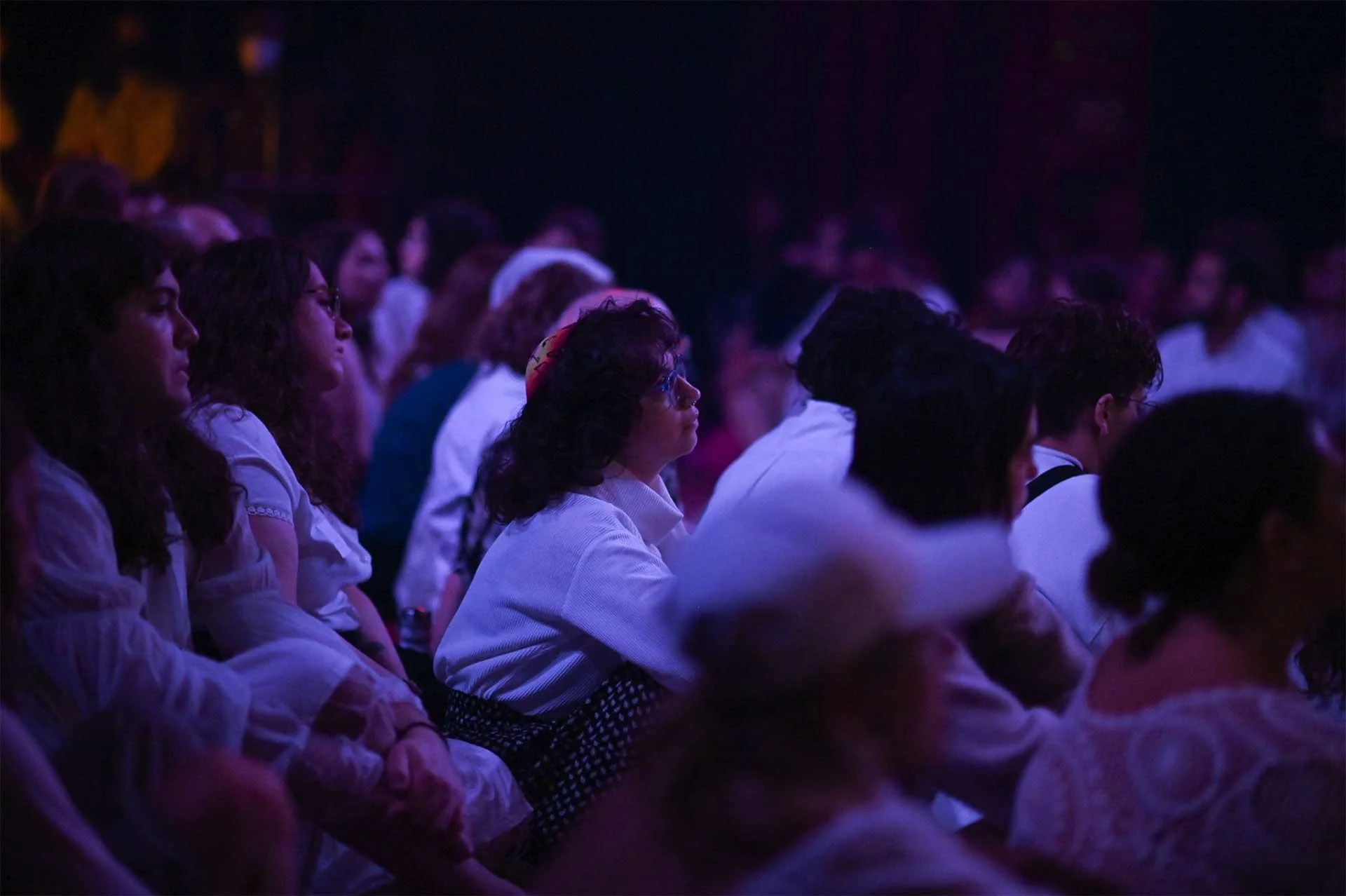A group of people sitting in a quiet audience, in a dark room at a Temple of the Stranger event