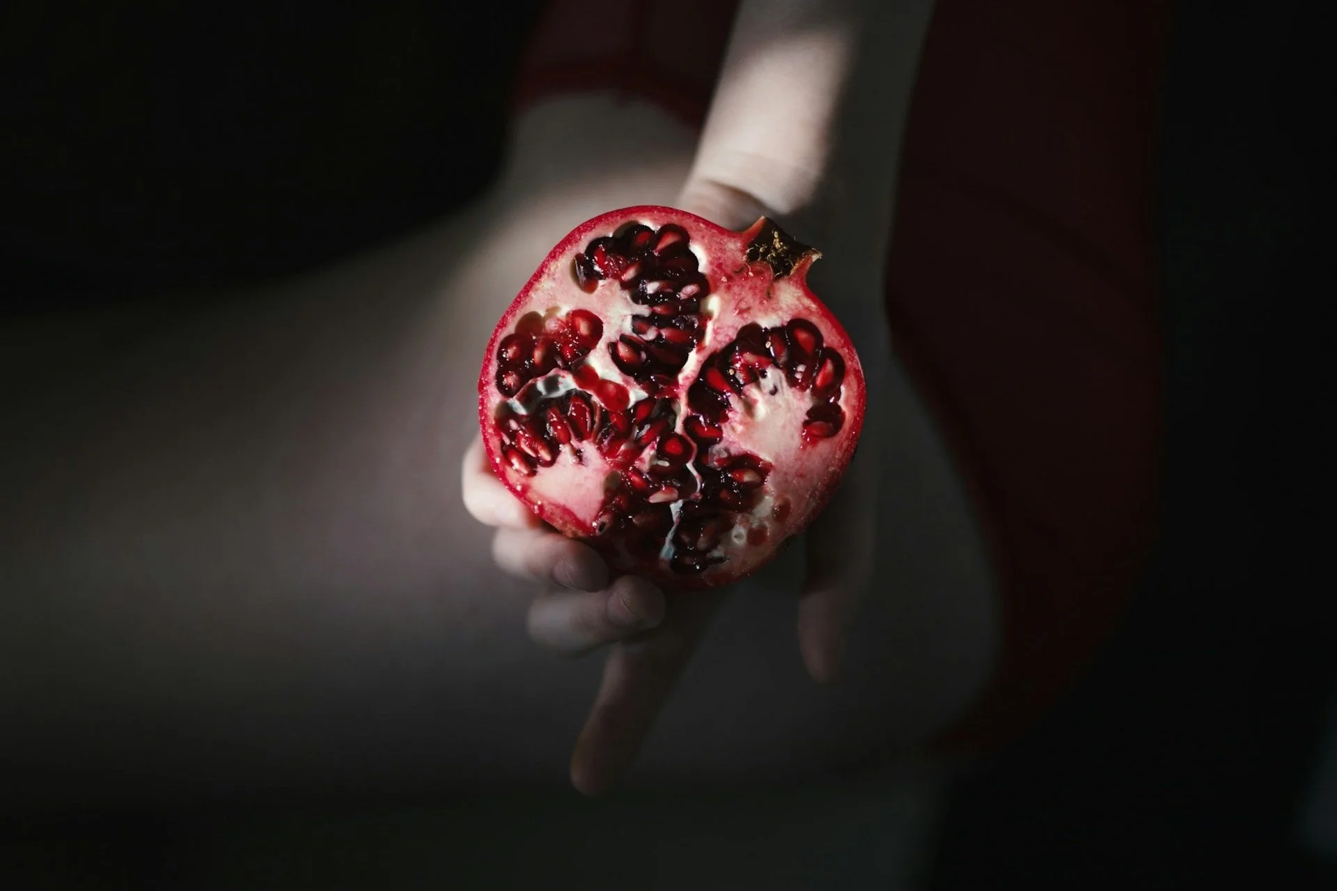 A hand holding up half a bright pomegranate with seeds intact