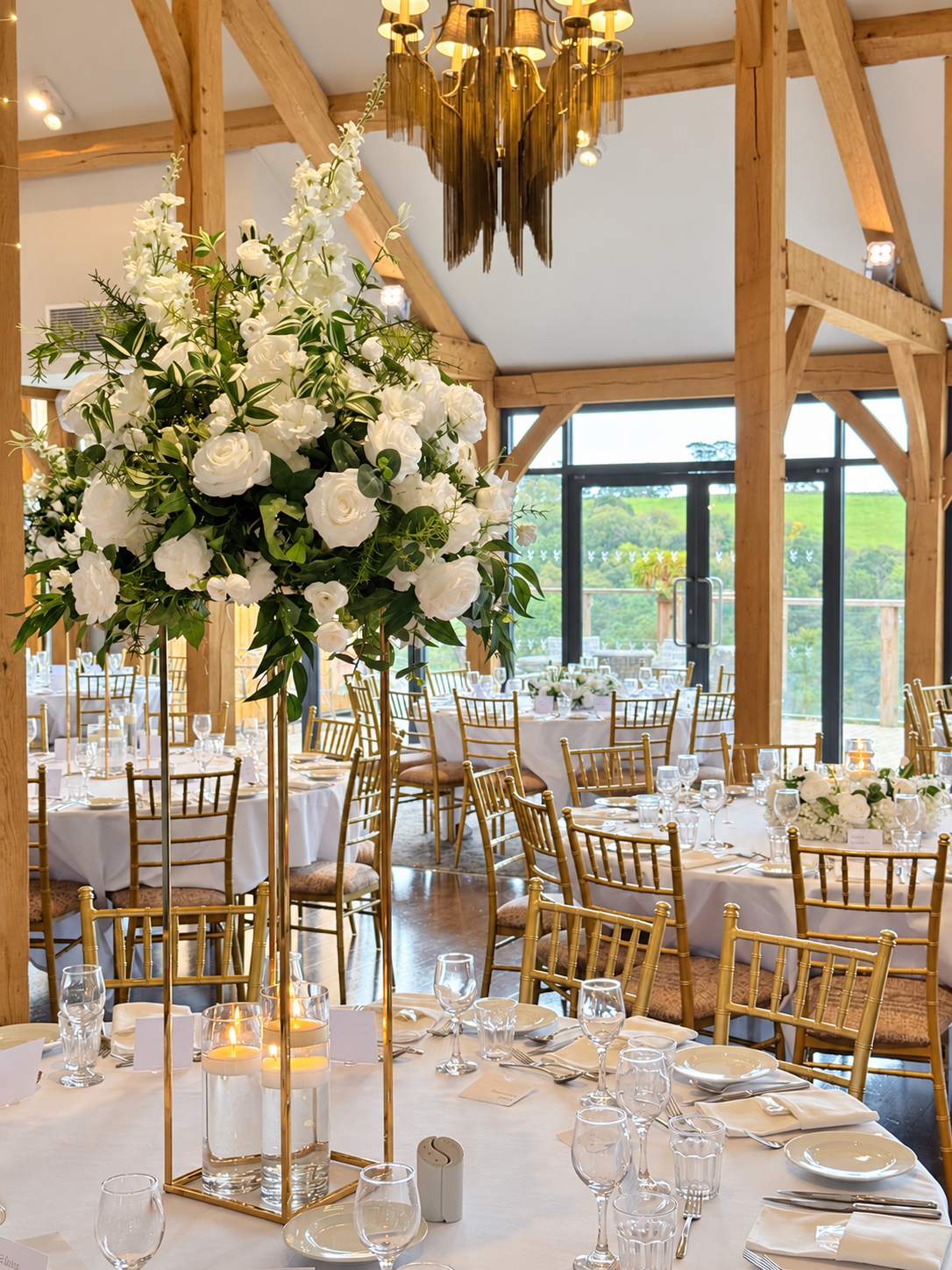 White and green silk floral wedding centrepiece with candles and gold chairs