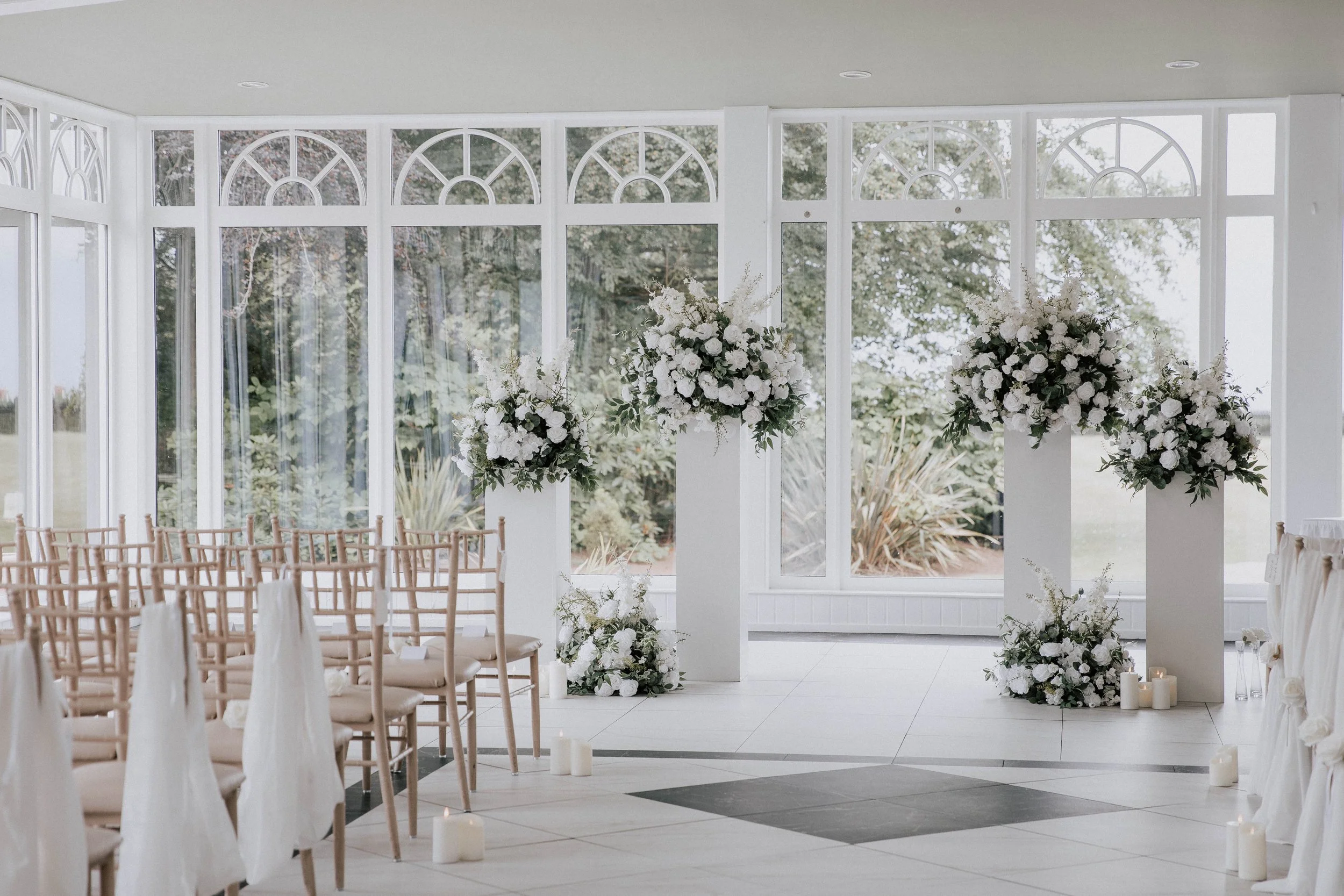 White silk floral arch and aisle arrangements in a bright wedding ceremony room