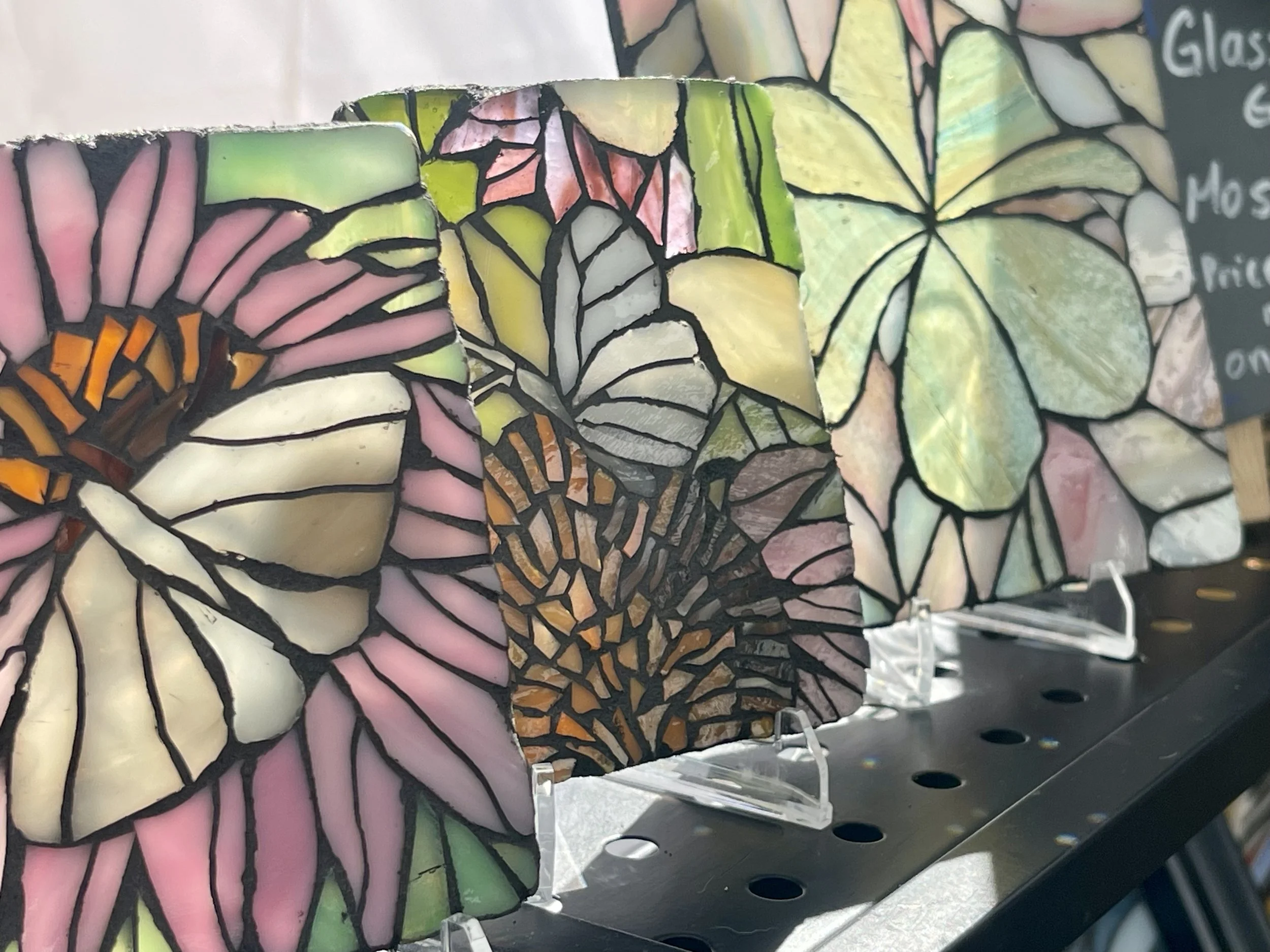 Colorful stained glass mosaic tiles featuring butterfly and leaf patterns displayed on a shelf.