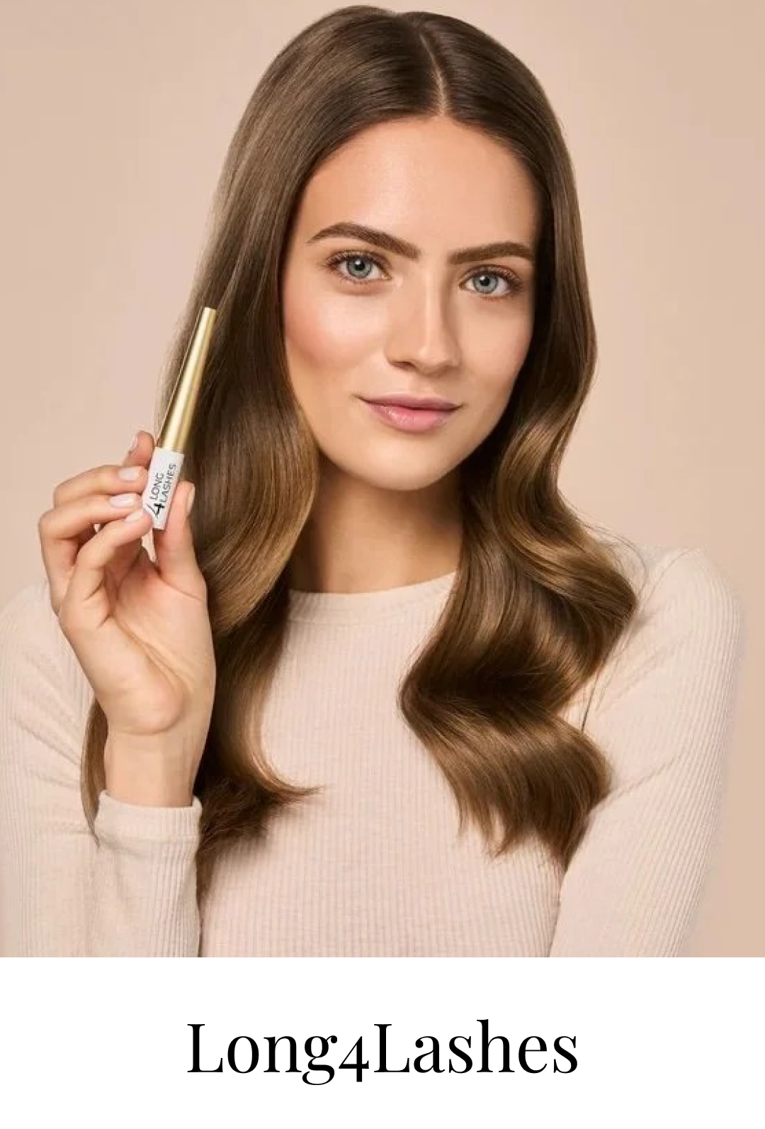 A woman with long, wavy brown hair holding a tube of Long4Lashes lash serum, smiling softly at the camera.