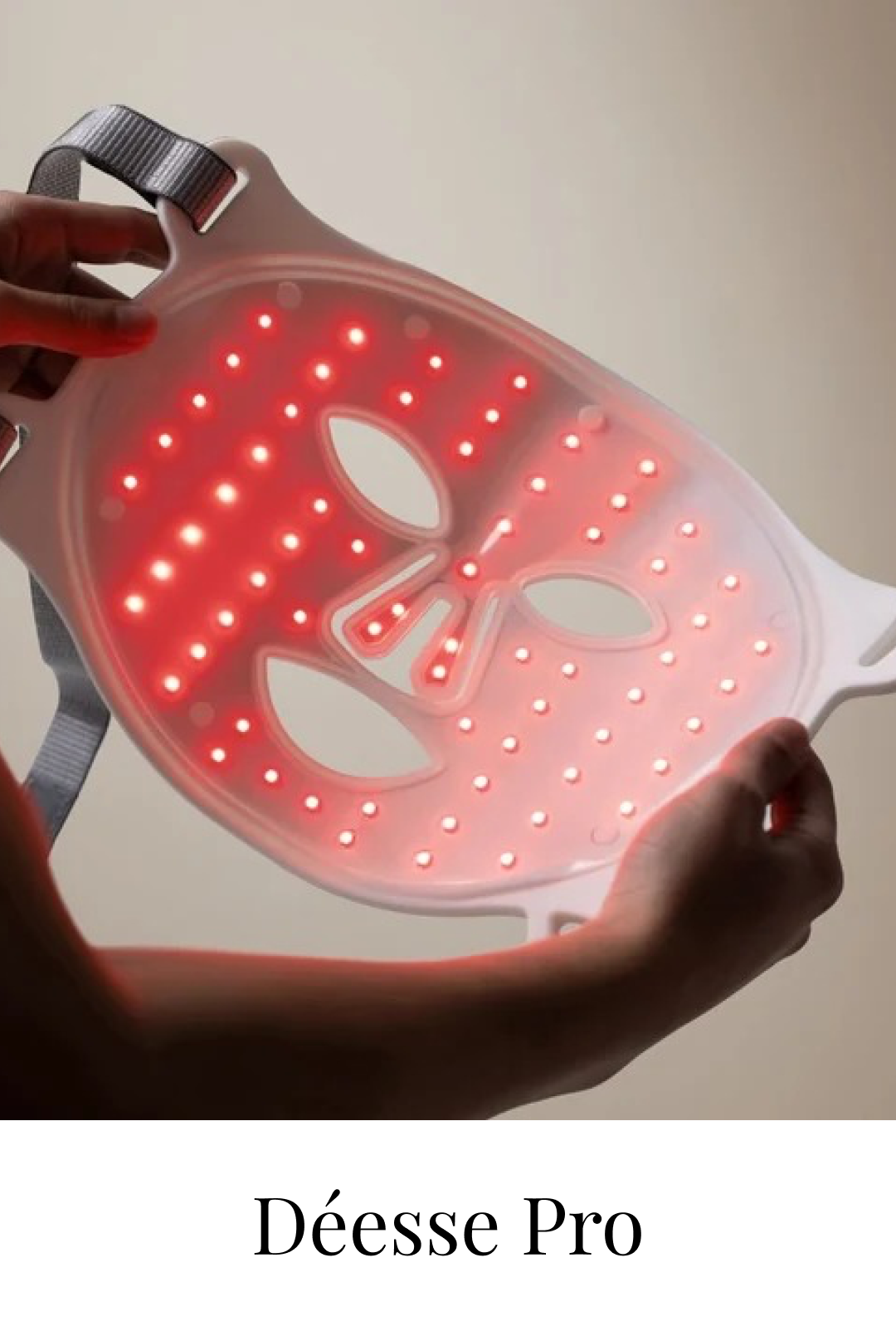 A portable red light therapy device called Déesse Pro, shaped like a mask, emitting red LED lights, being held with both hands against a plain background.