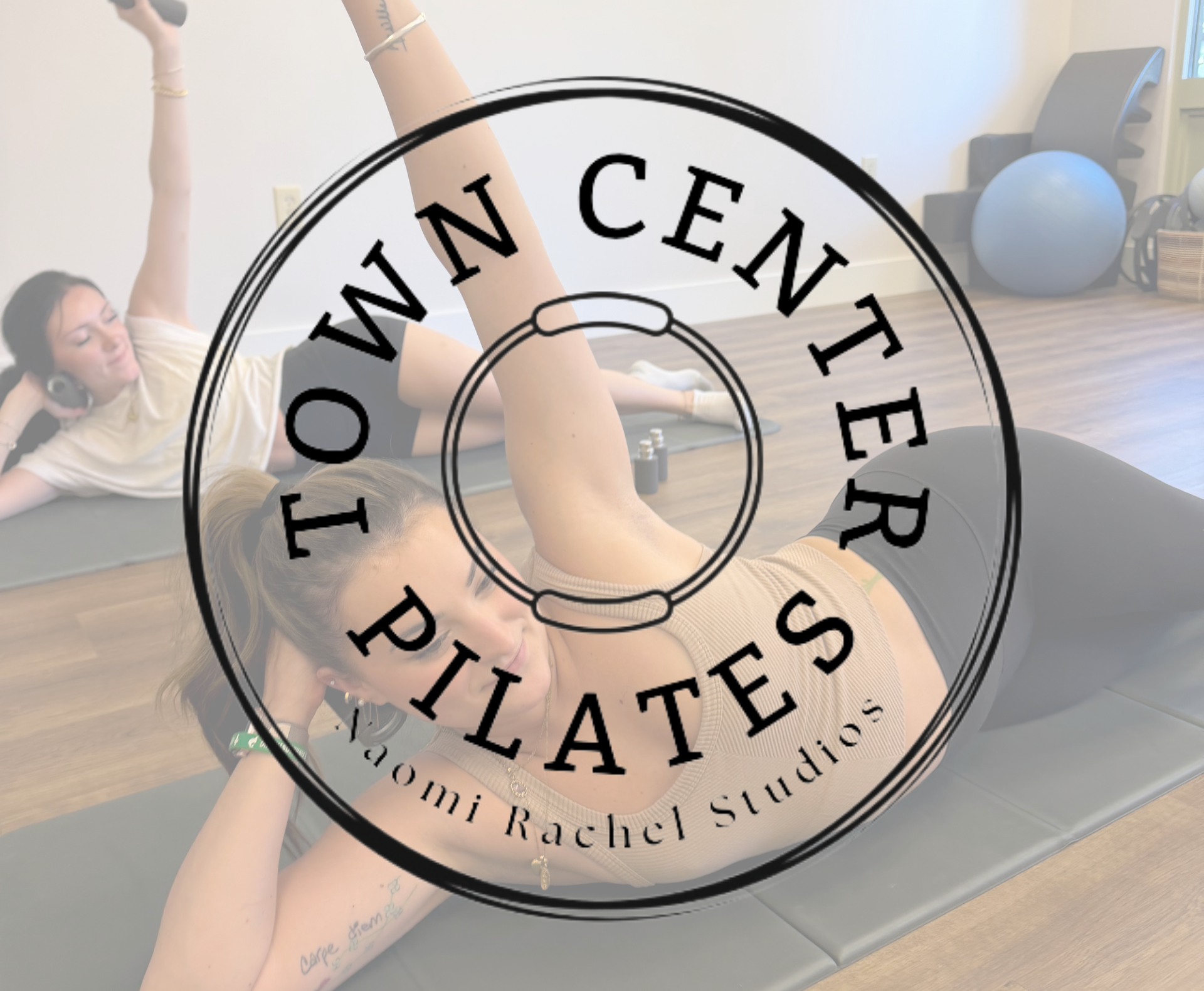 Women exercising on yoga mats in a fitness studio, with exercise equipment including a stability ball and weights in the background.