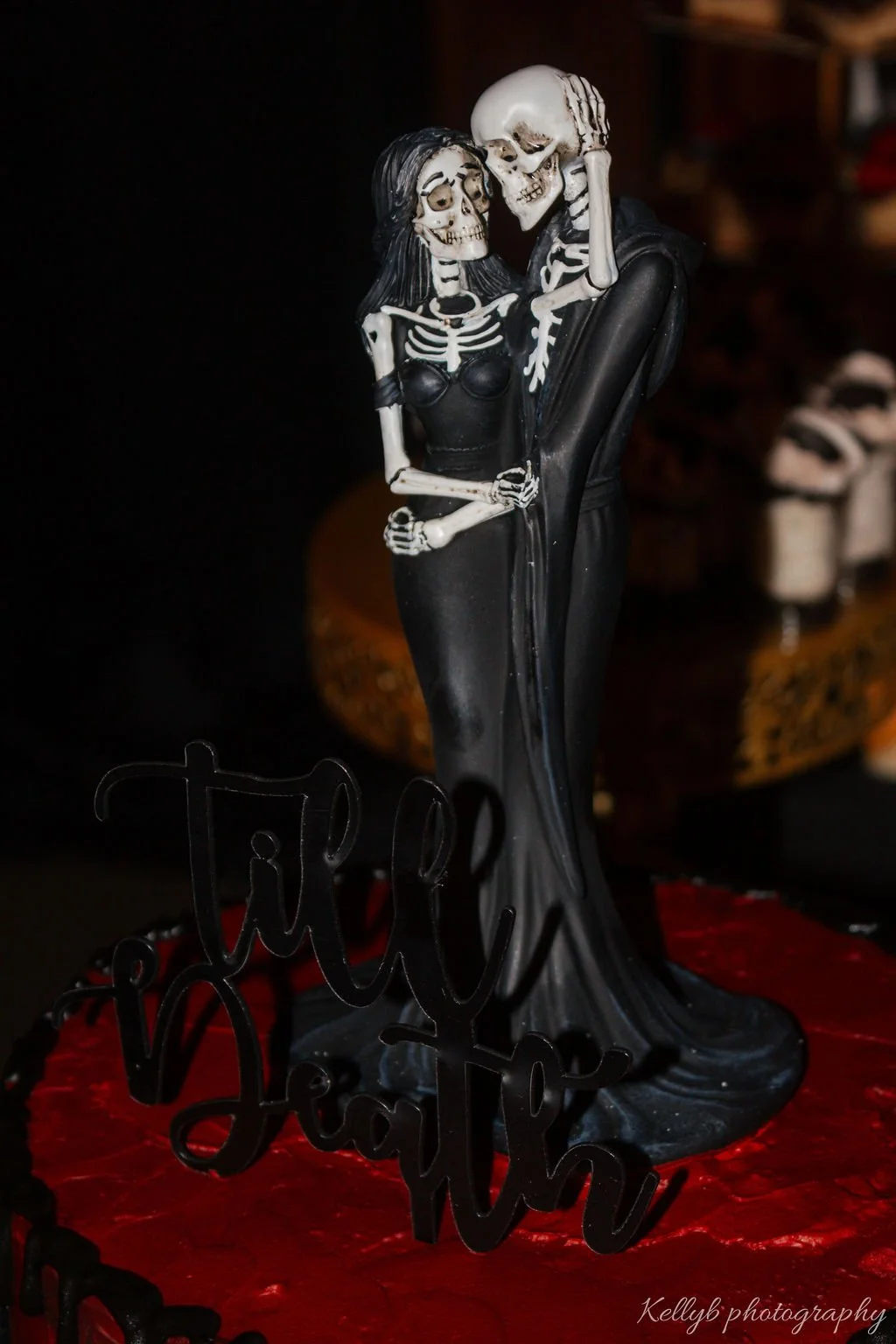 A Halloween-themed figurine of a skeleton couple dressed as a bride and groom, with the skeletons embracing, and a black 'Trick' sign at the base.