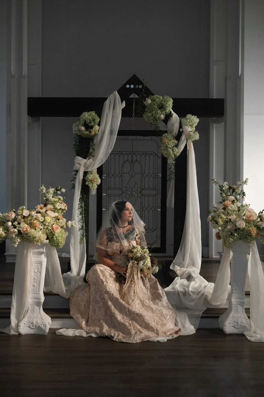 Bridal portrait in a wedding setting with floral arrangements and drapery.