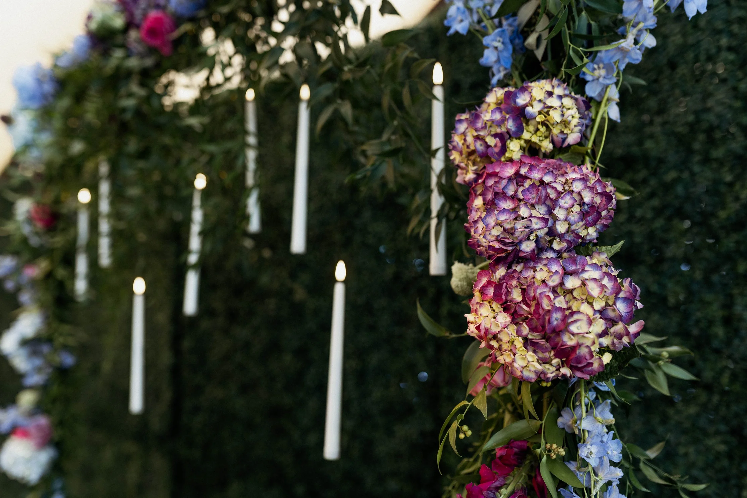 Flowers arranged on a wall with hanging white candles or lights in the background.