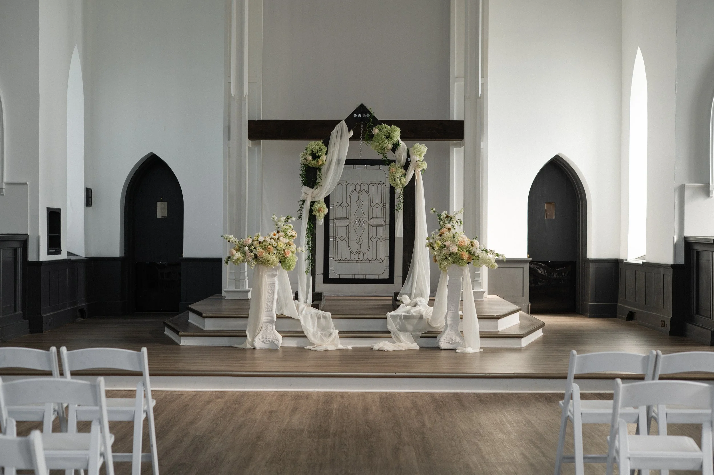 A decorated church for a wedding with white drapes and floral arrangements on the altar.