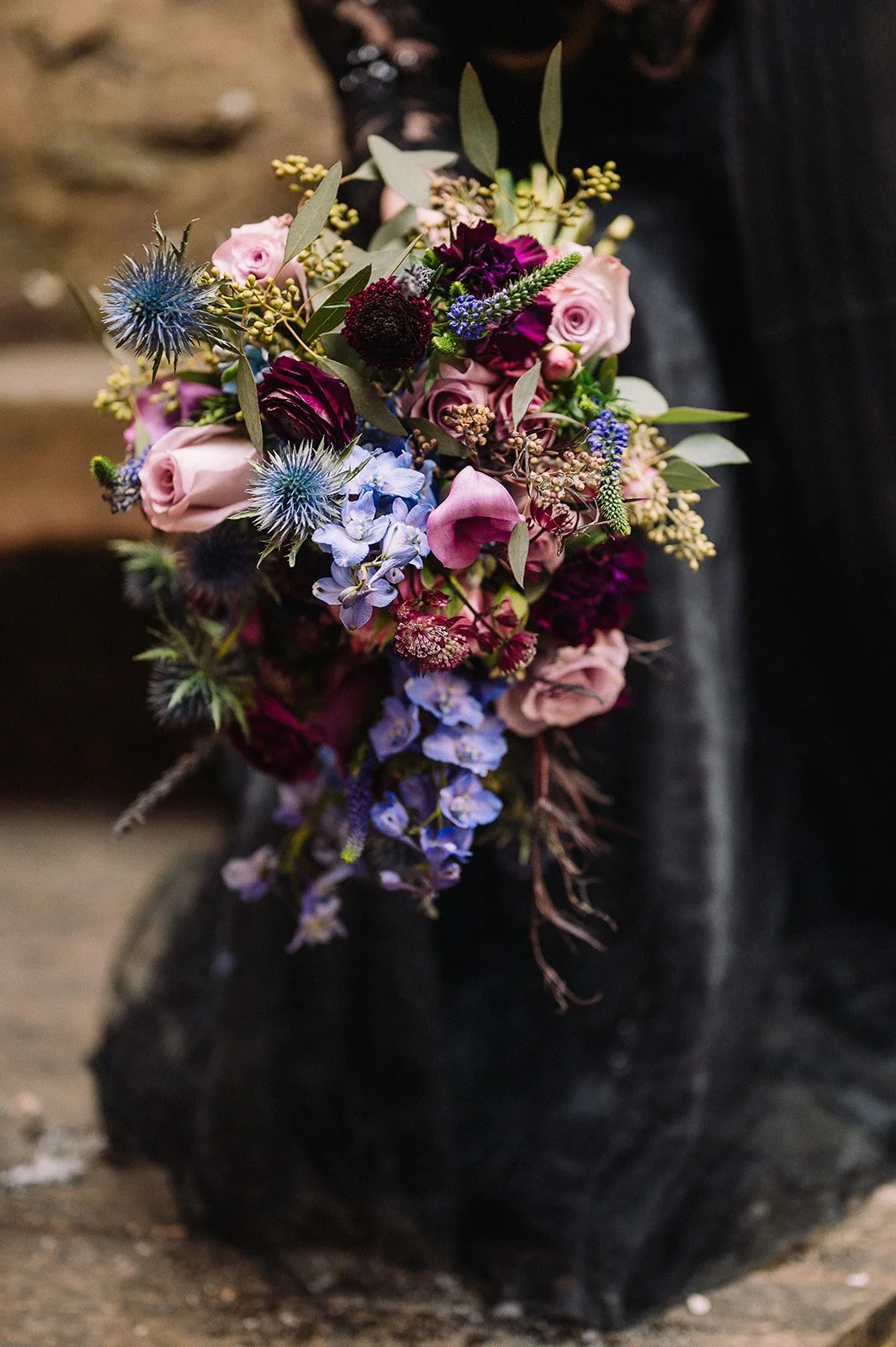 A beautiful floral bouquet with pink, purple, blue, and green flowers held in a black paper wrapper.
