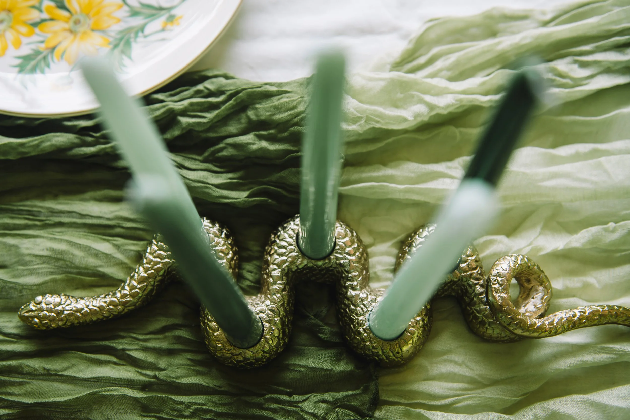 Decorative gold snake-shaped candle holder with three green candles on a textured green cloth.