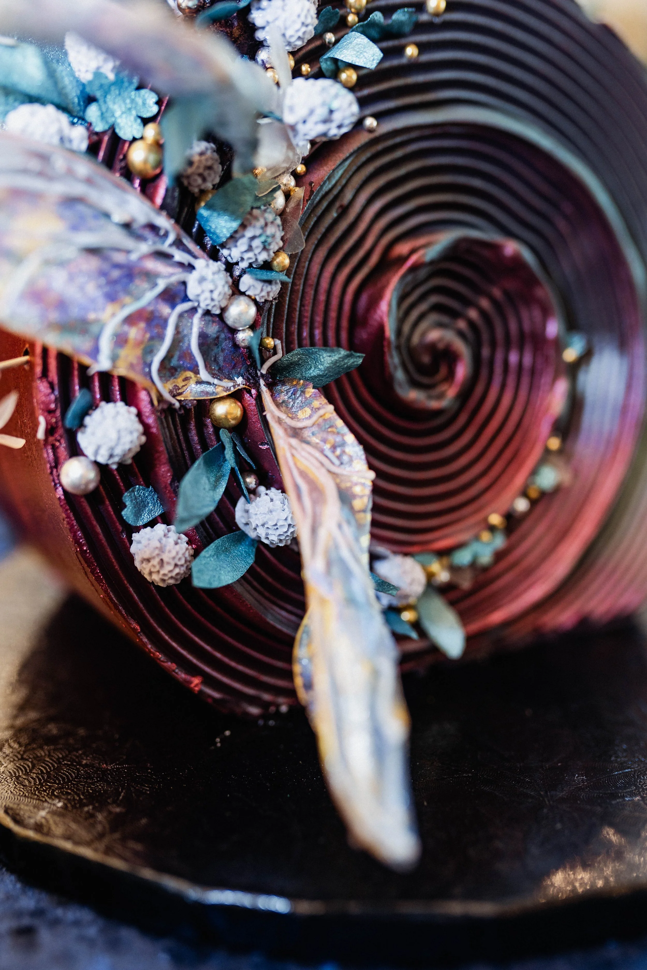 Close-up of a rolled decorative fabric or paper with intricate embellishments including leaves, pearls, and textured white accents, on a dark surface.