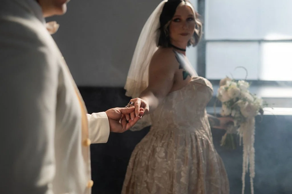Bride holding groom's hand at their wedding ceremony, with bouquet of flowers in the background.
