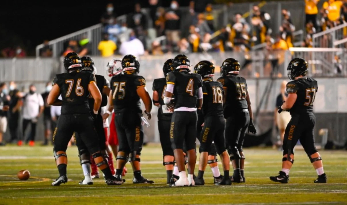 High school football team in black uniforms strategizing on field during a game.