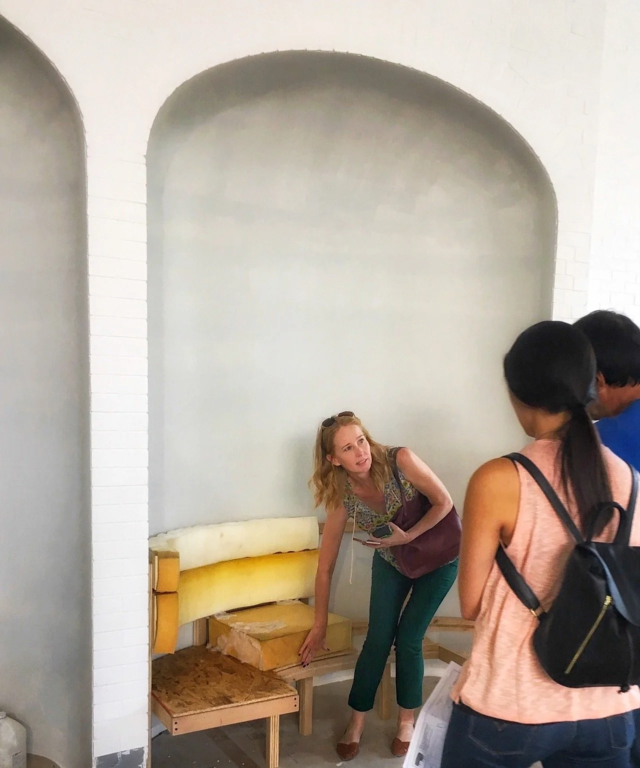 Interior scene with a woman showing a partially constructed bench to two people.