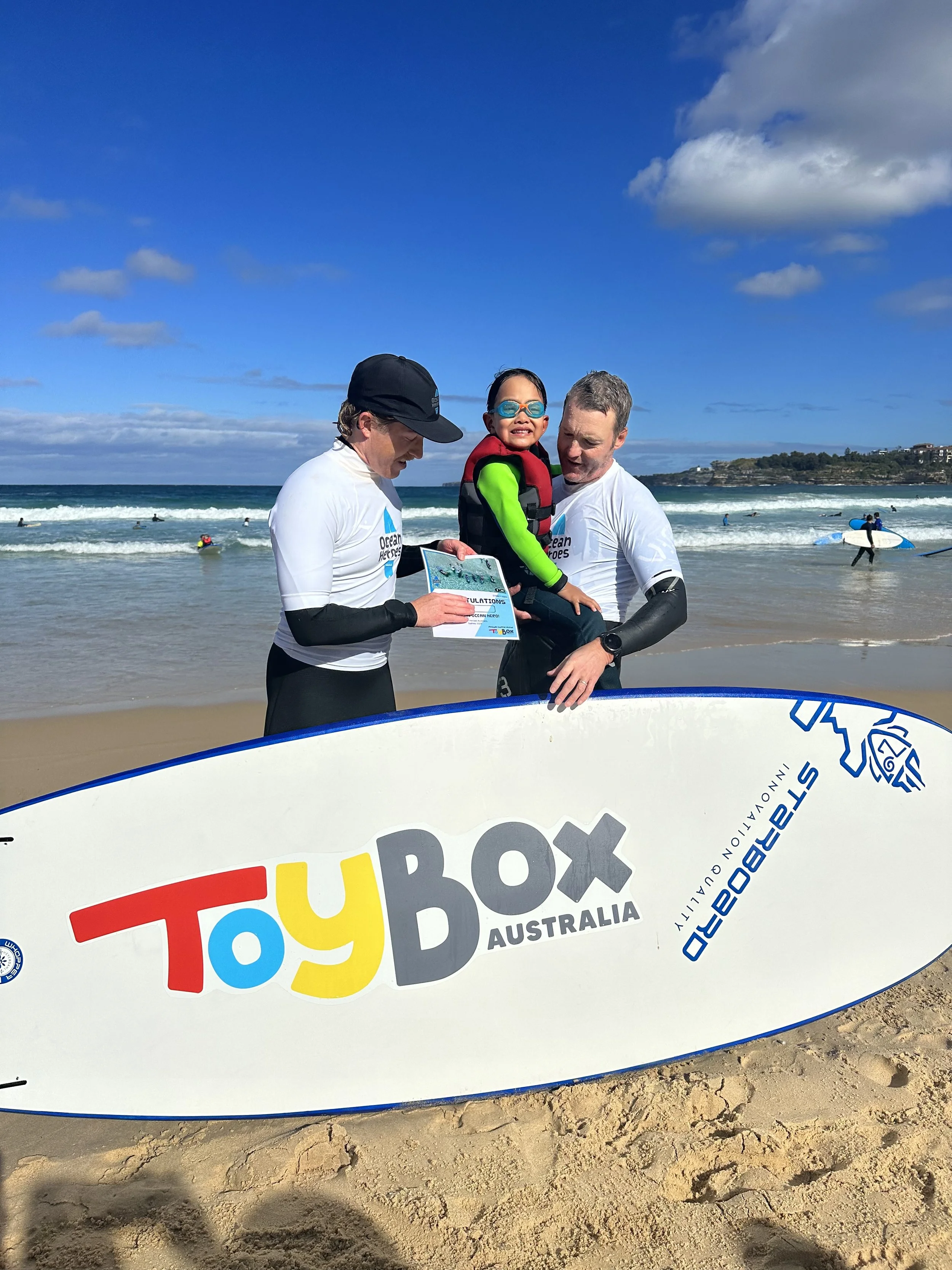 2 surfers holding child in front of surfboard and beach