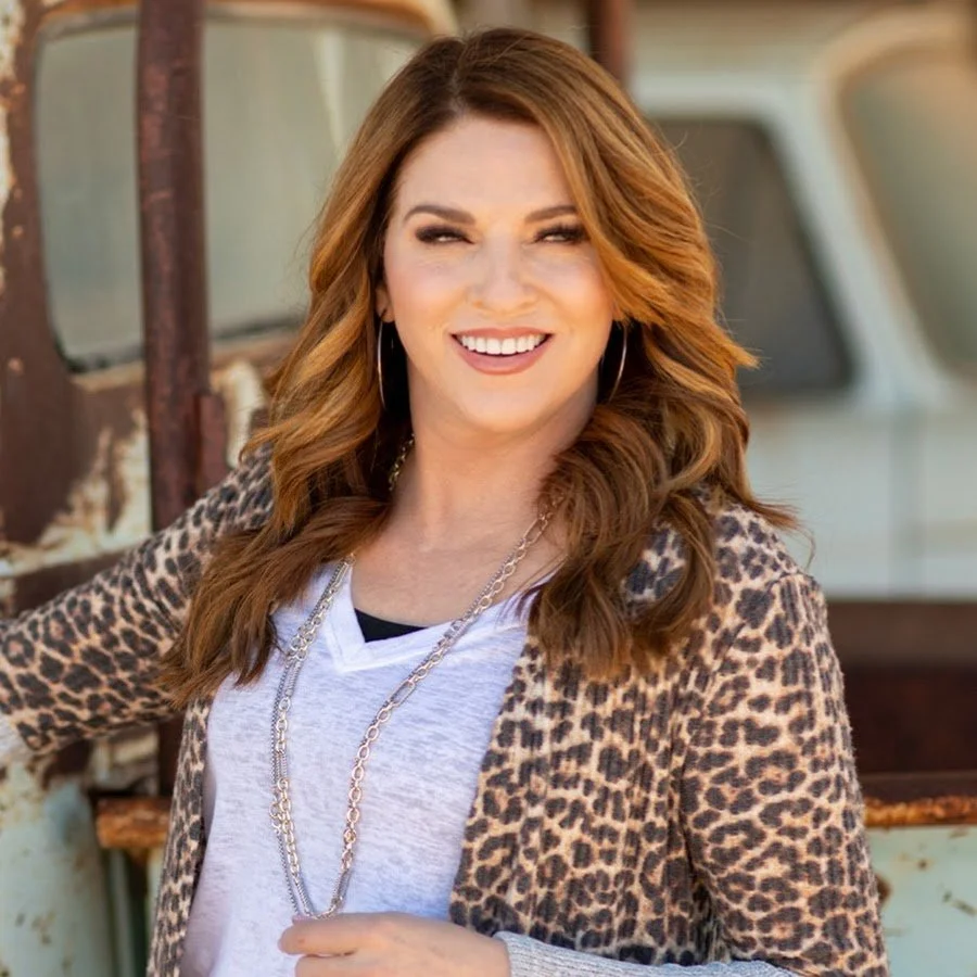 Smiling woman with brown hair wearing a leopard print cardigan and necklace standing outdoors.