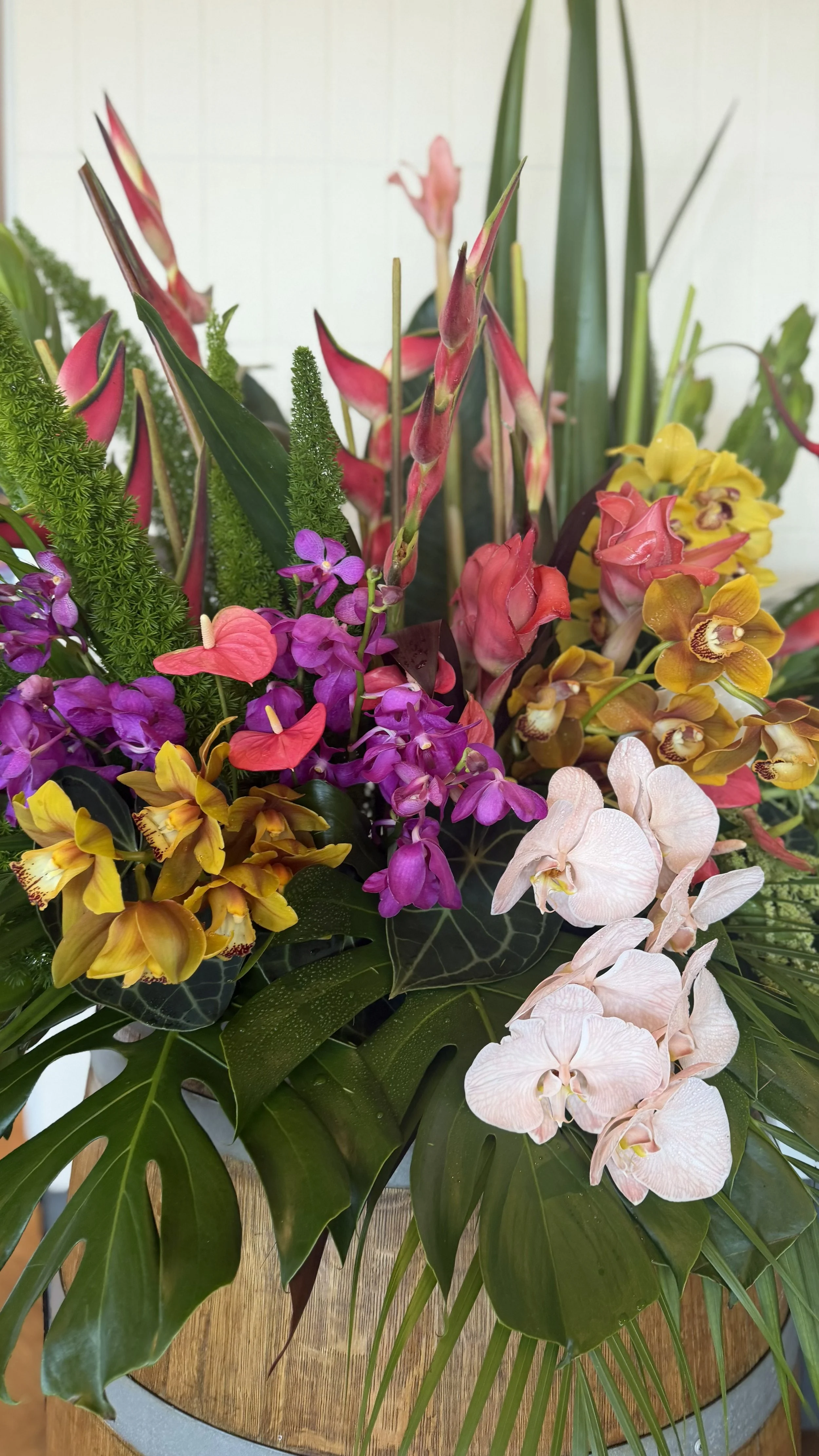 A bouquet of various flowers including pink ginger, purple orchids, yellow orchids, white orchids, and green foliage arranged in a pot.
