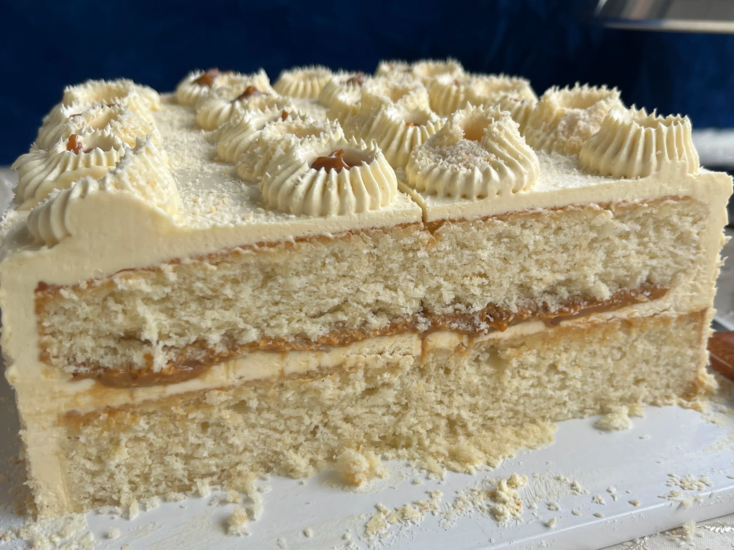 A sliced coconut layered cake with cream cheese frosting, dulce de leche, and decorated with piped cream rosettes, and shredded coconut on top.