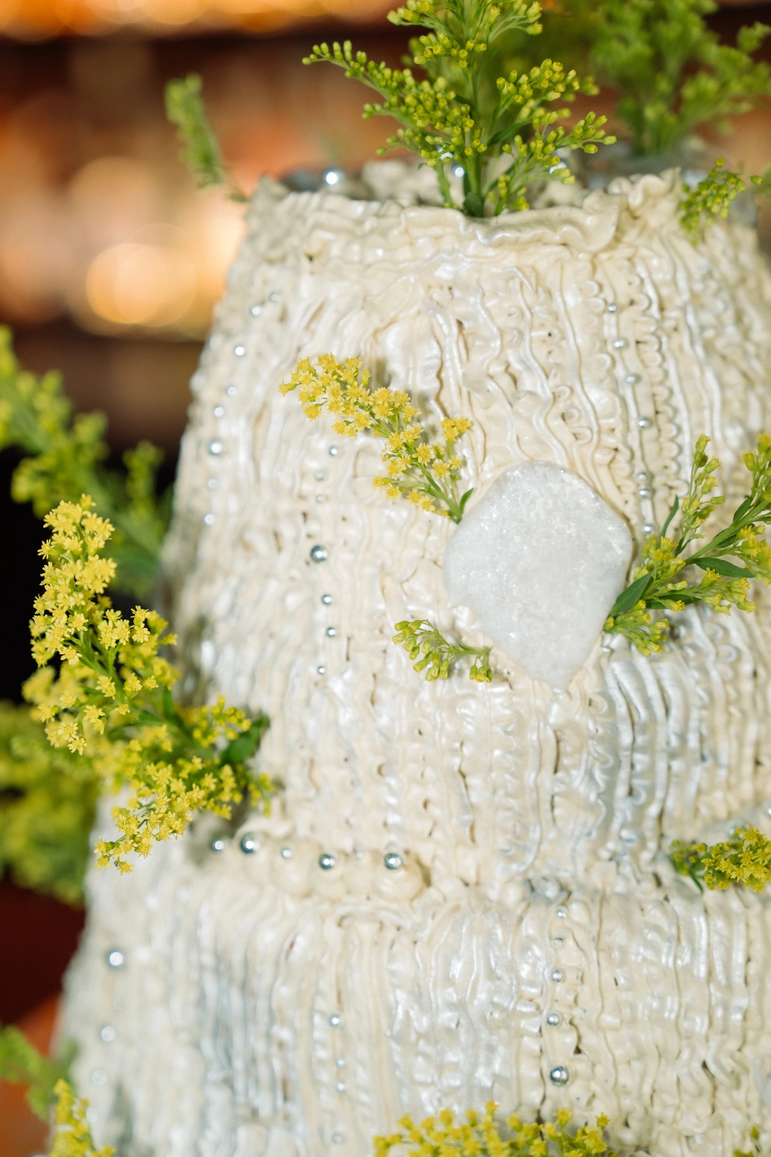 Close-up of a decorated wedding cake with white icing, edible silver beads, and small yellow flowers.