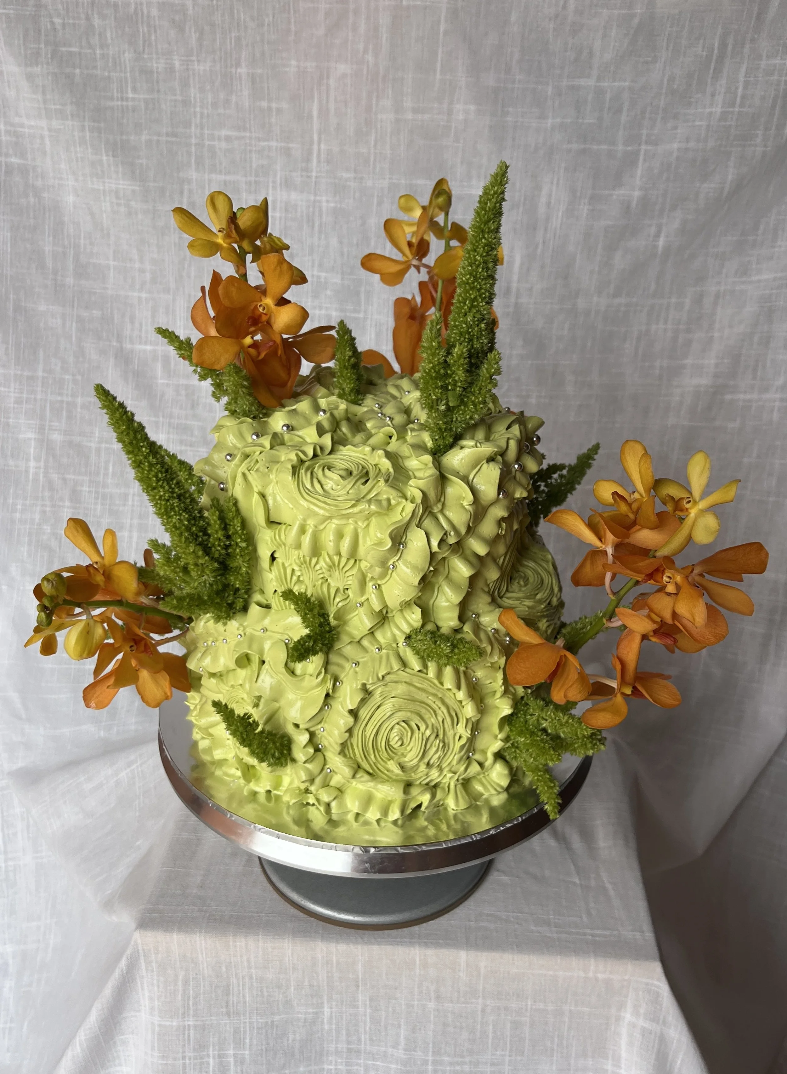 A floral arrangement with orange orchids, green foliage, and decorative silver beads on a silver cake stand.