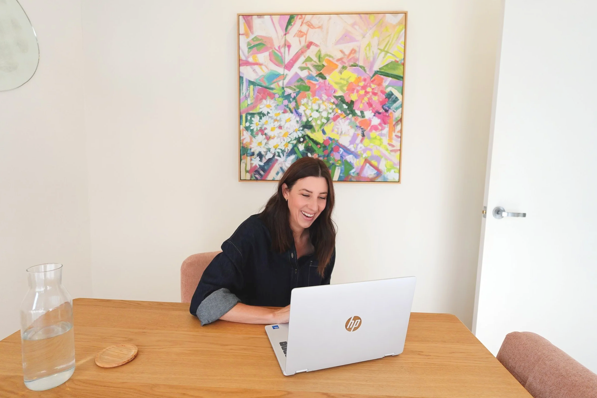 Top-down view of a silver Apple MacBook and a glass of ice water on a light-colored surface, with sunlight casting shadows.