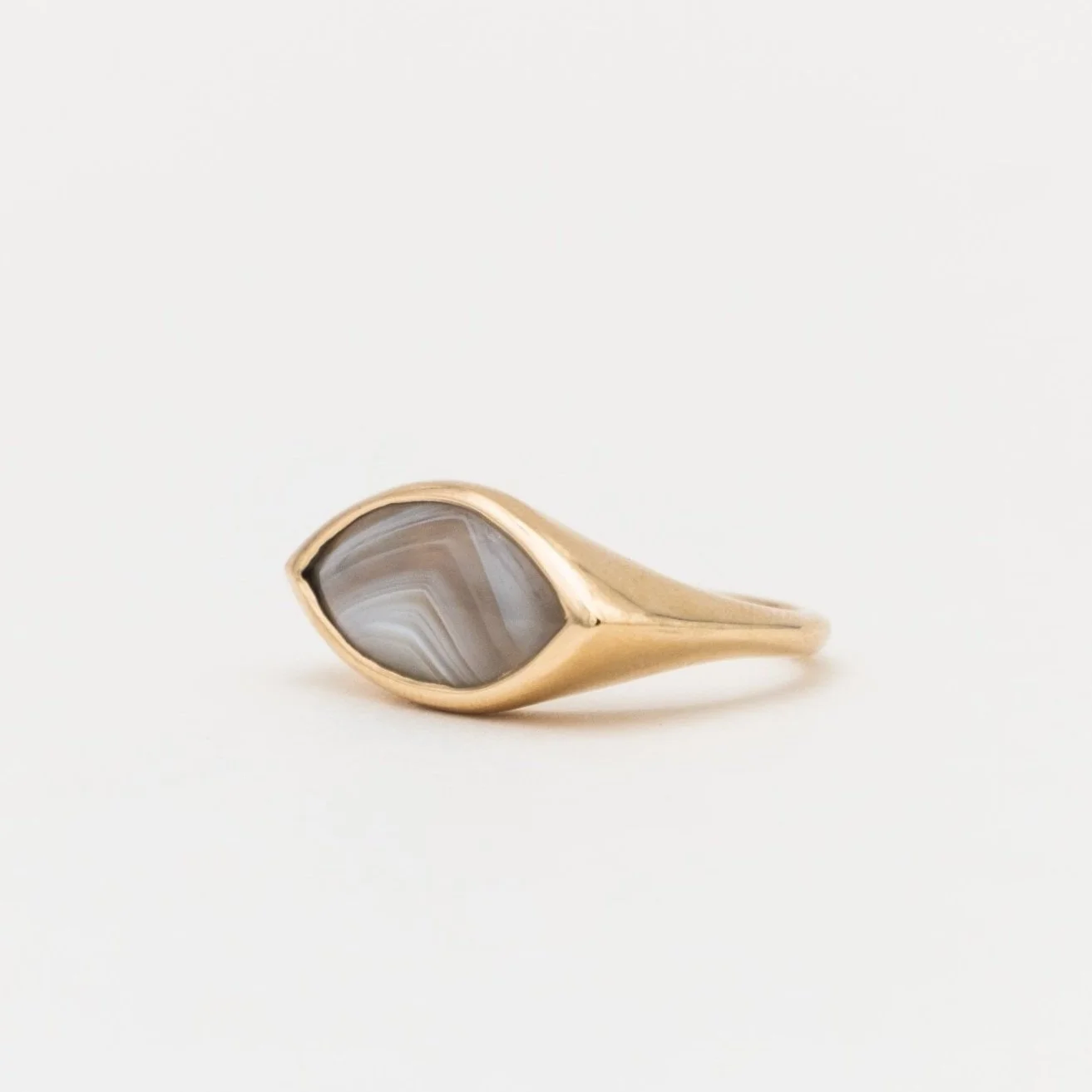 Gold ring with a marbled gray and white stone set in a bezel setting, isolated on a white background.