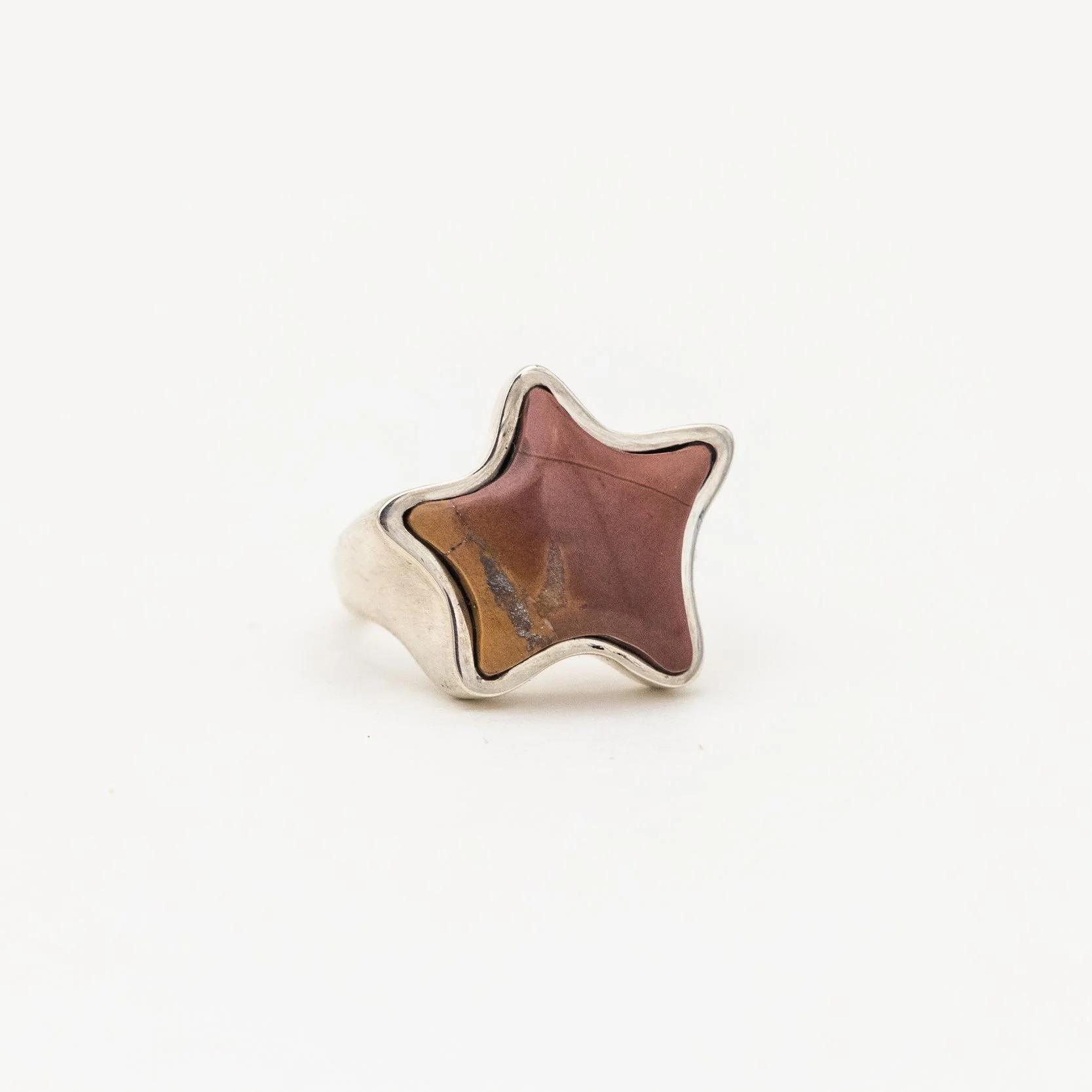 Star-shaped ring with a pink and brown stone in a silver setting on a white background.