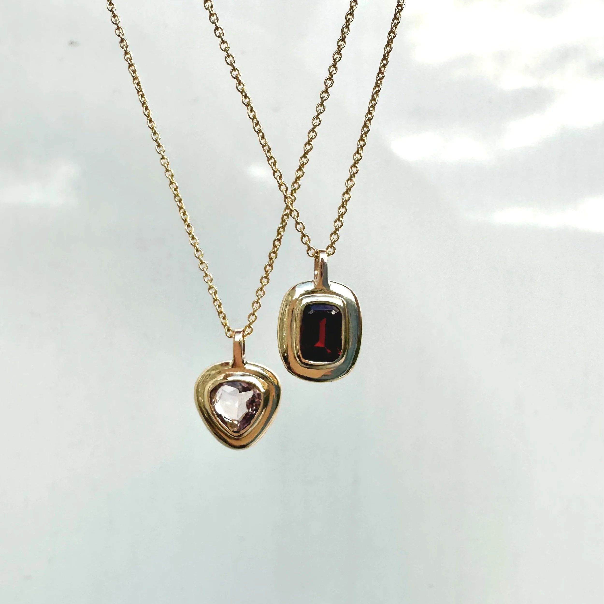 Two gold necklaces each with a pendant; one pendant has a heart-shaped clear gemstone, and the other has a rectangular black gemstone.